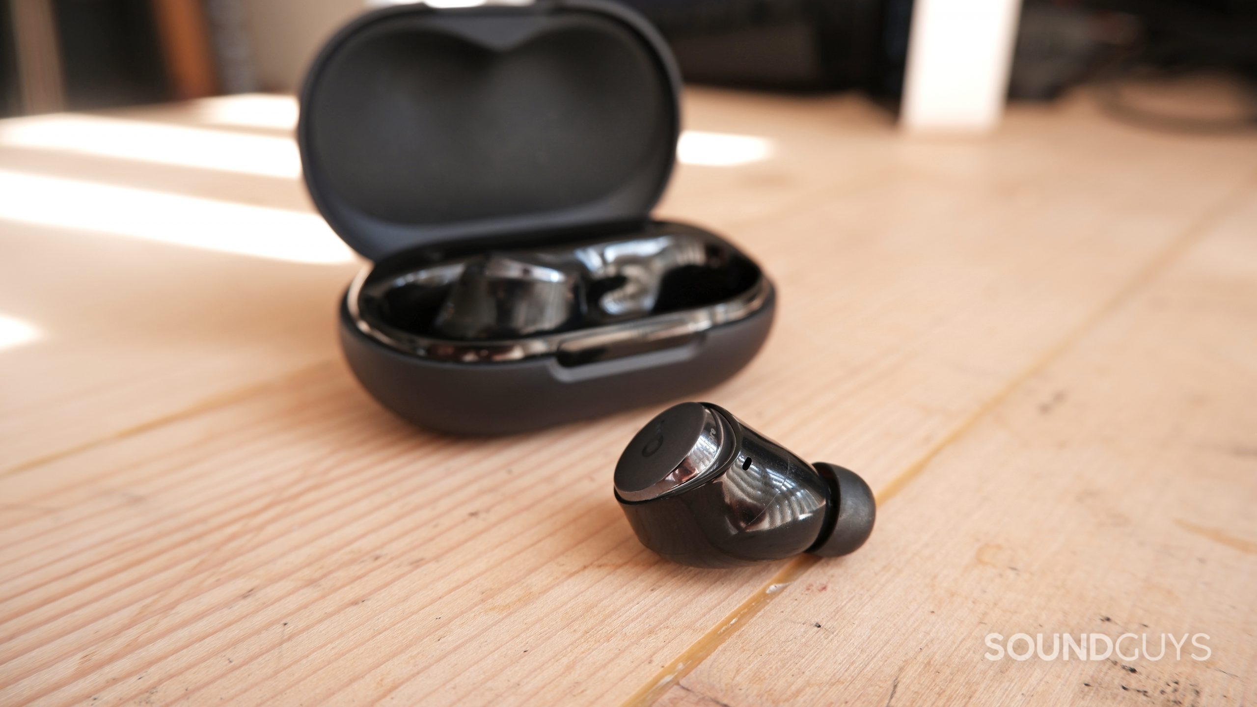 One earbud of the Anker Soundcore Space A40 sitting on a table outside the open case.