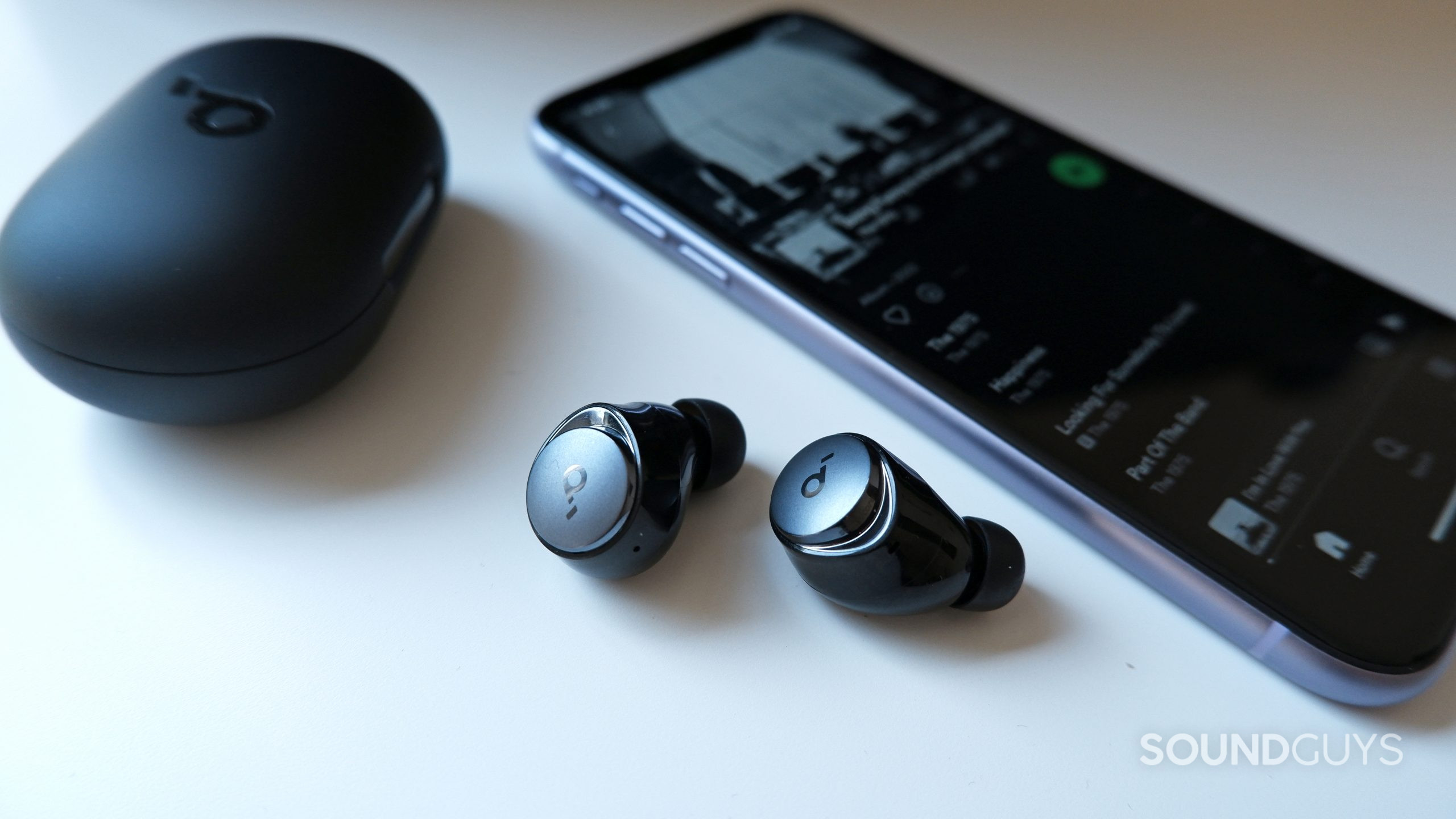 The Anker Soundcore Space A40 earbuds beside a phone with spotify open.