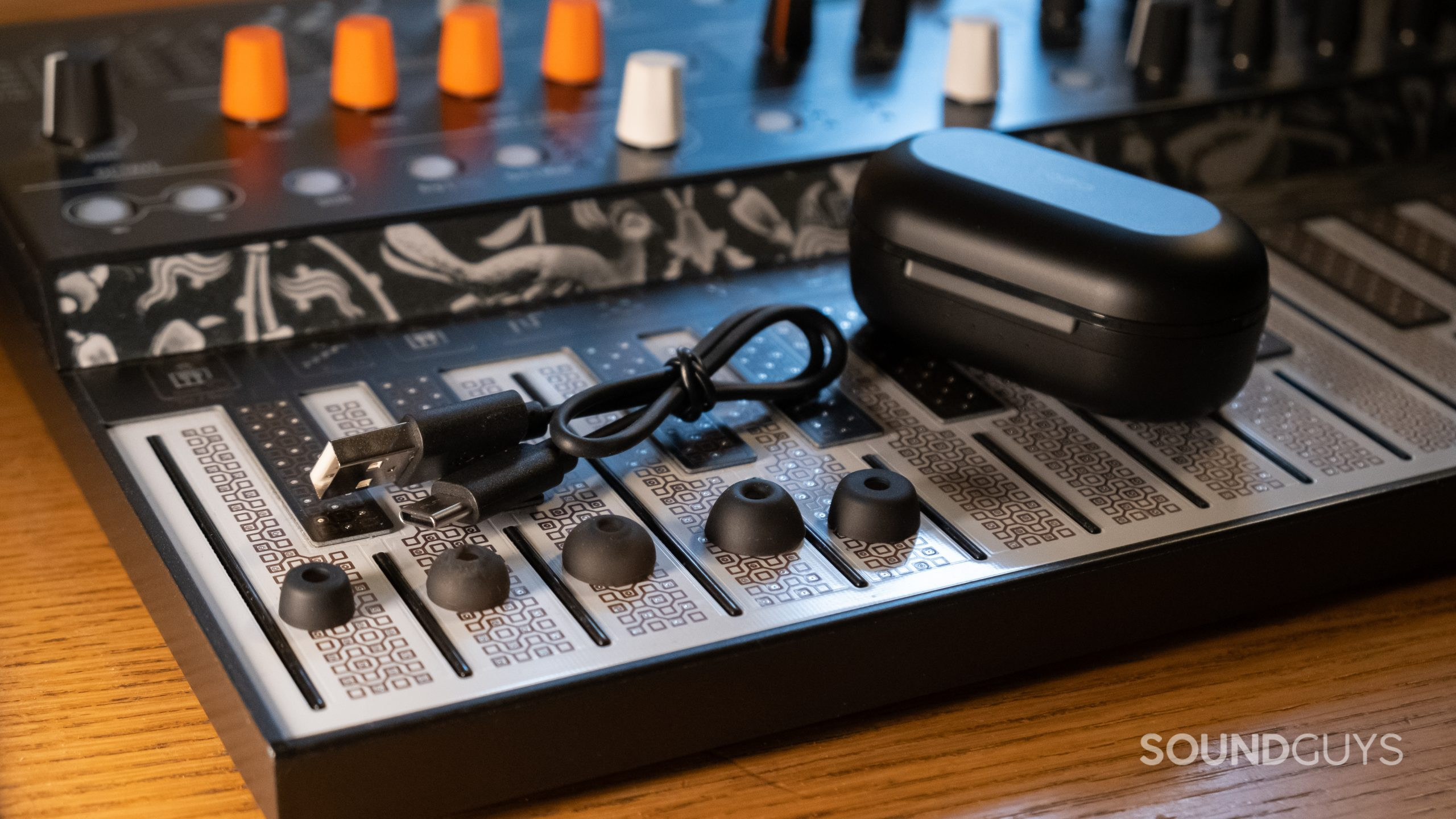 On a synthesizer keyboard rest the ear tips, USB-C cables, and case of the TOZO NC9.