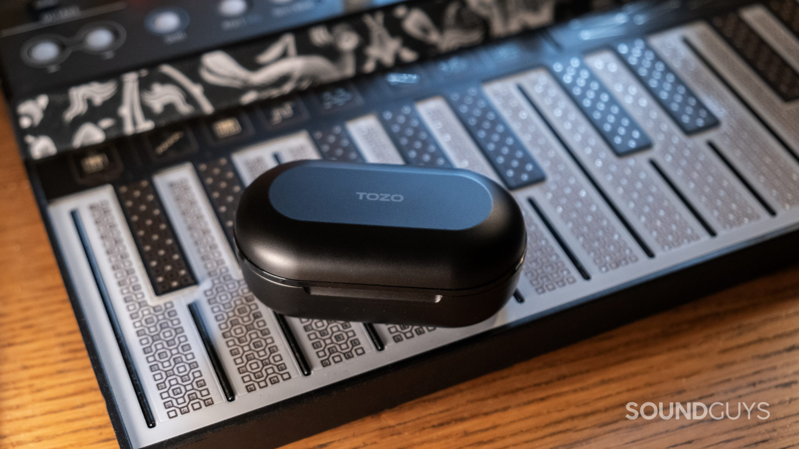 The pill shaped case of the TOZO NC9 in black rests on the keyboard of a synth.