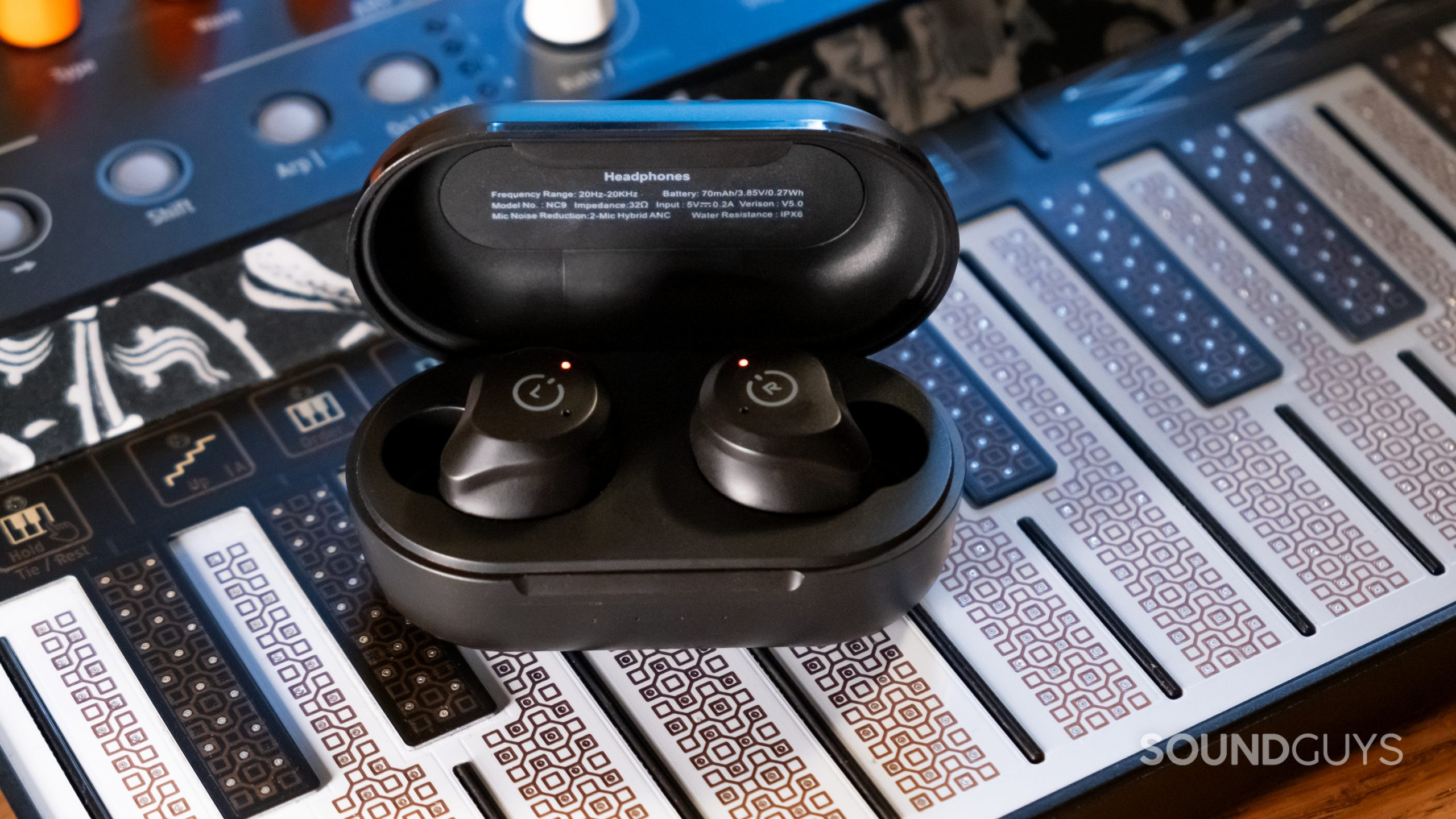 The TOZO NC9 wireless earbuds rest in the open case on top of a synthesizer.