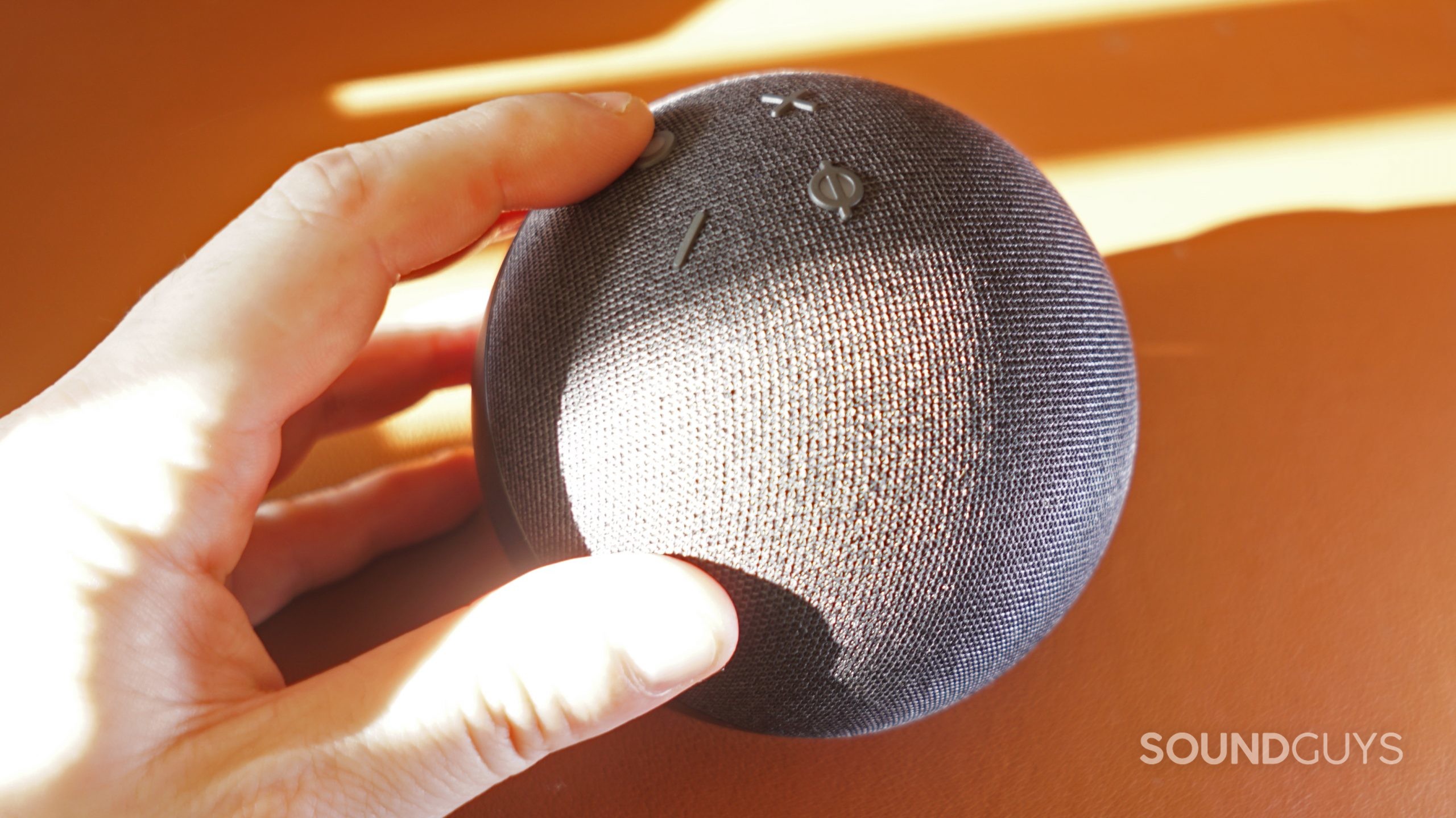 Amazon-Echo-Dot-(5th-gen)-hand The Amazon Echo Dot (5th Gen) sits on an orange leather surface, and a hand is on its controls.