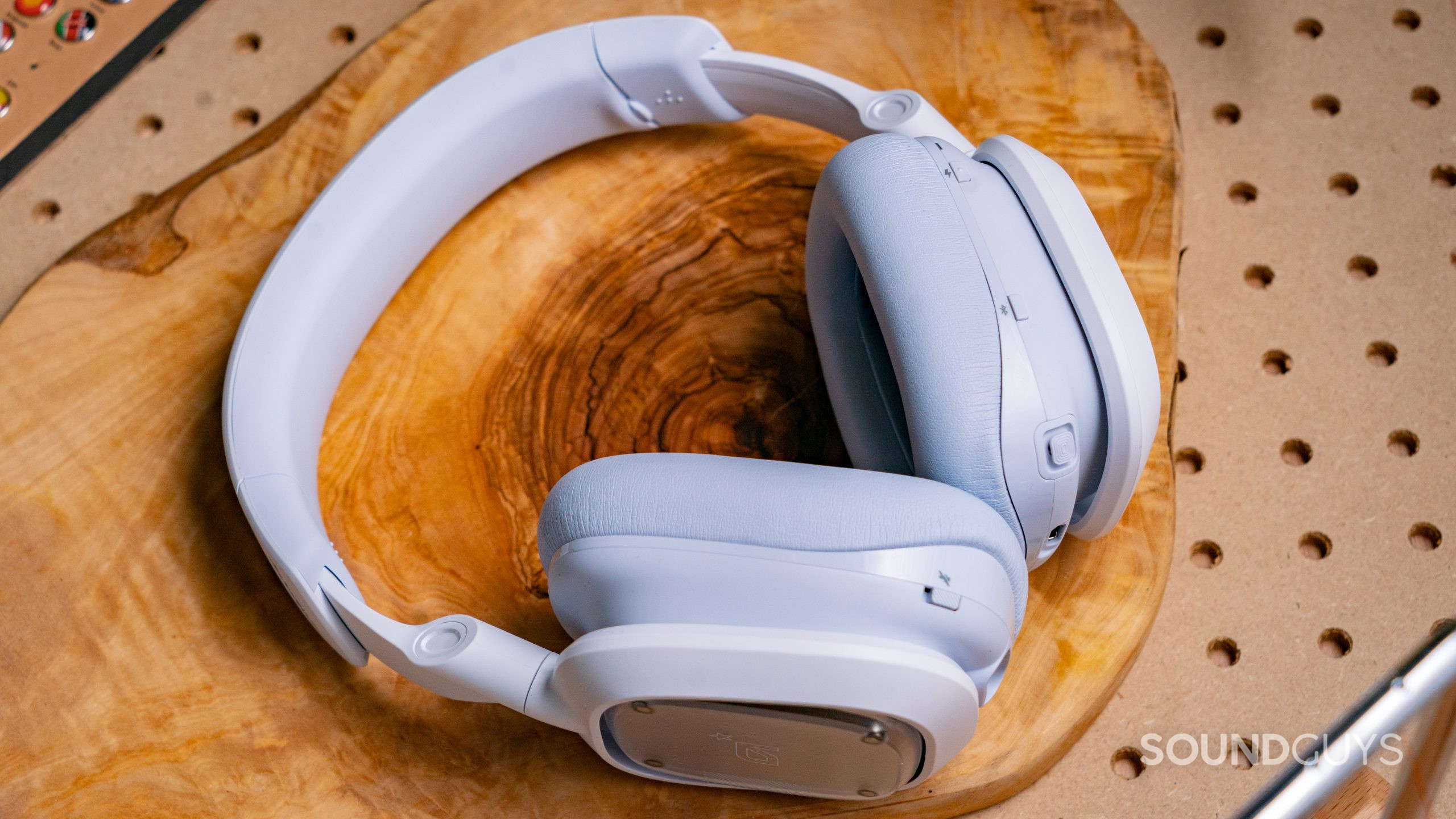 The Astro A30 gaming headset laying on a wooden surface, showing the mute button on the left ear cup, and the power button, Bluetooth button, and multifunction rocker on the right ear cup.
