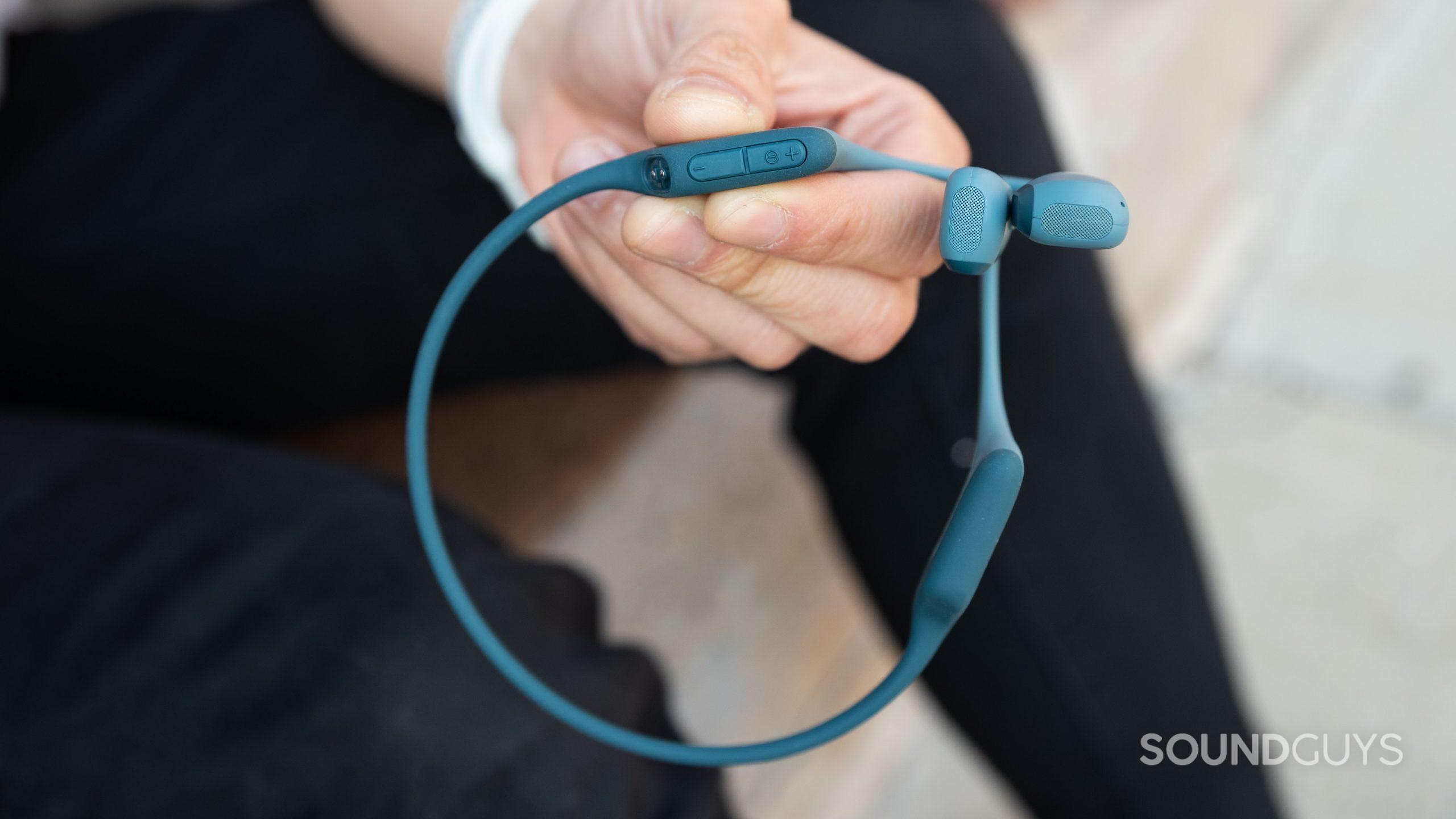 A hand holds the Shokz OpenRun Pro bone conduction headphones to show the volume controls.