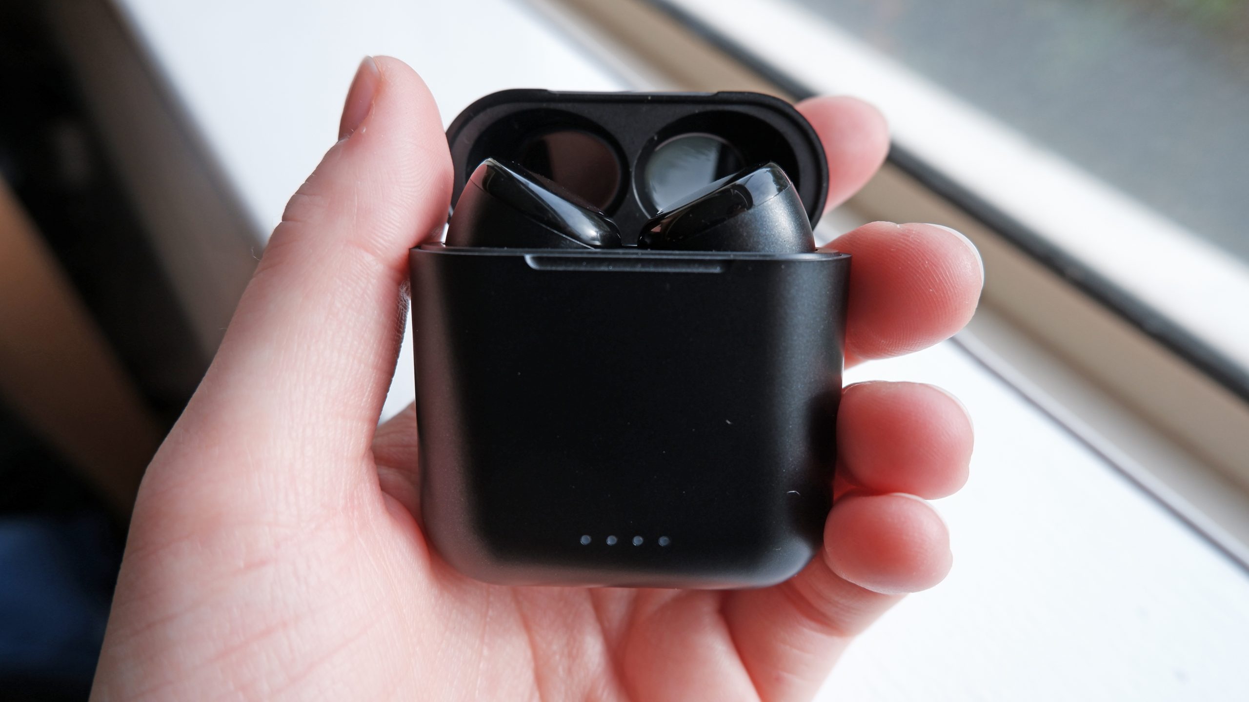The TOZO T6 case open with the earbuds inside, the case being held by a hand.