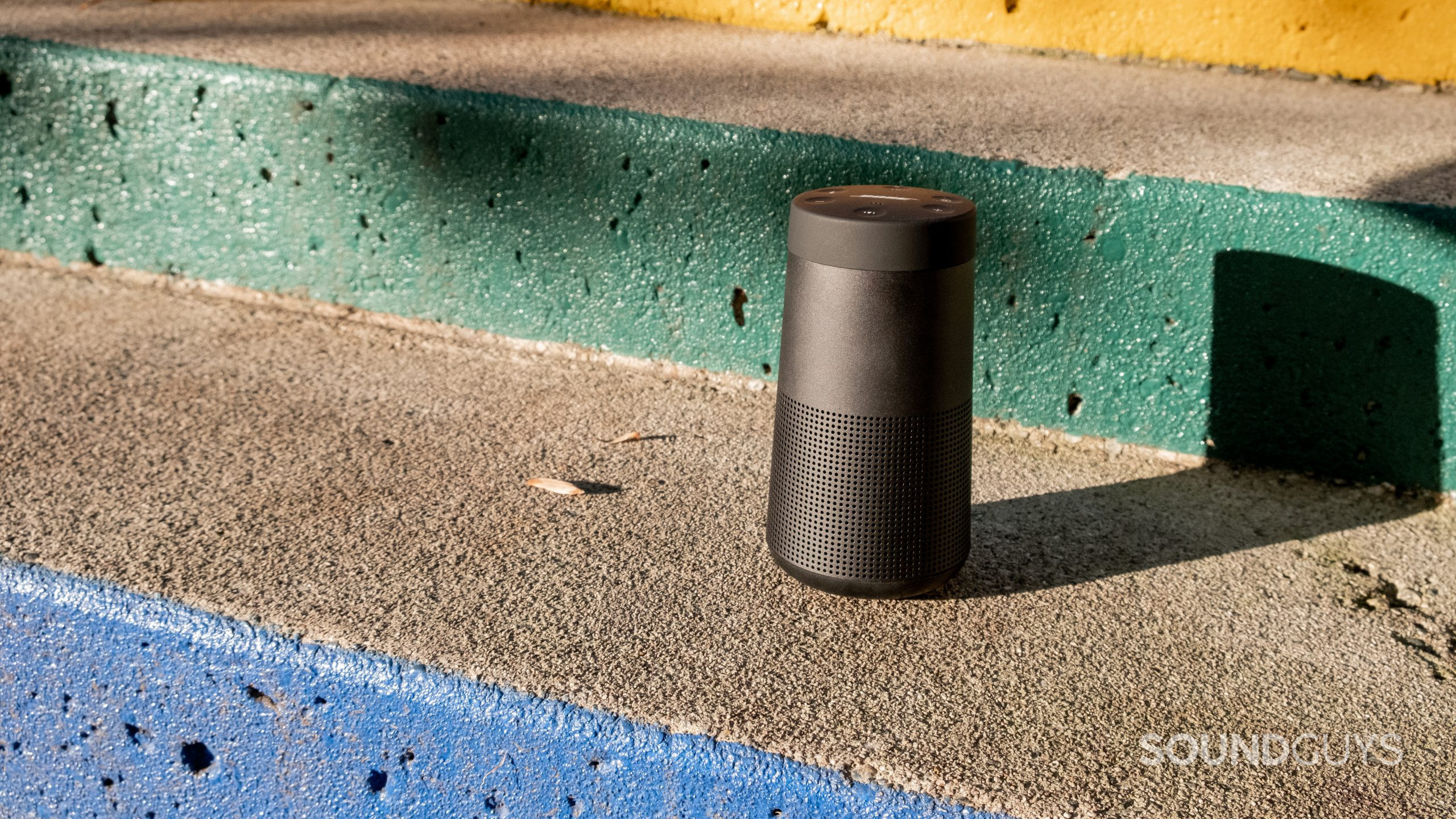 The Bose SoundLink Revolve II sits on a concrete stair with the concrete stairs painted yellow, green, and blue.