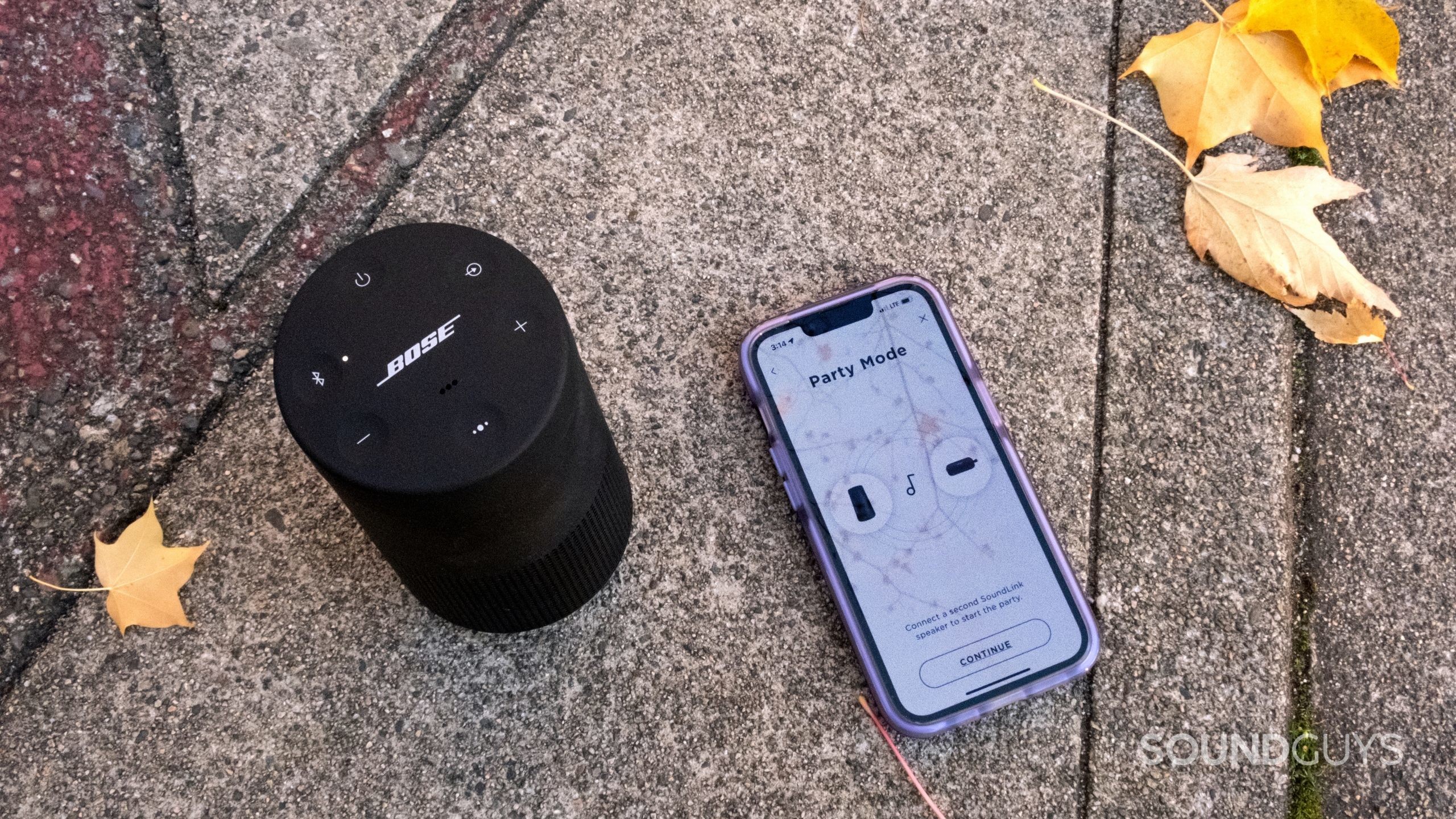 On concrete the Bose SoundLink Revolve II is shown from above displaying the controls next to an iPhone showing Party Mode in the Bose Connect app.