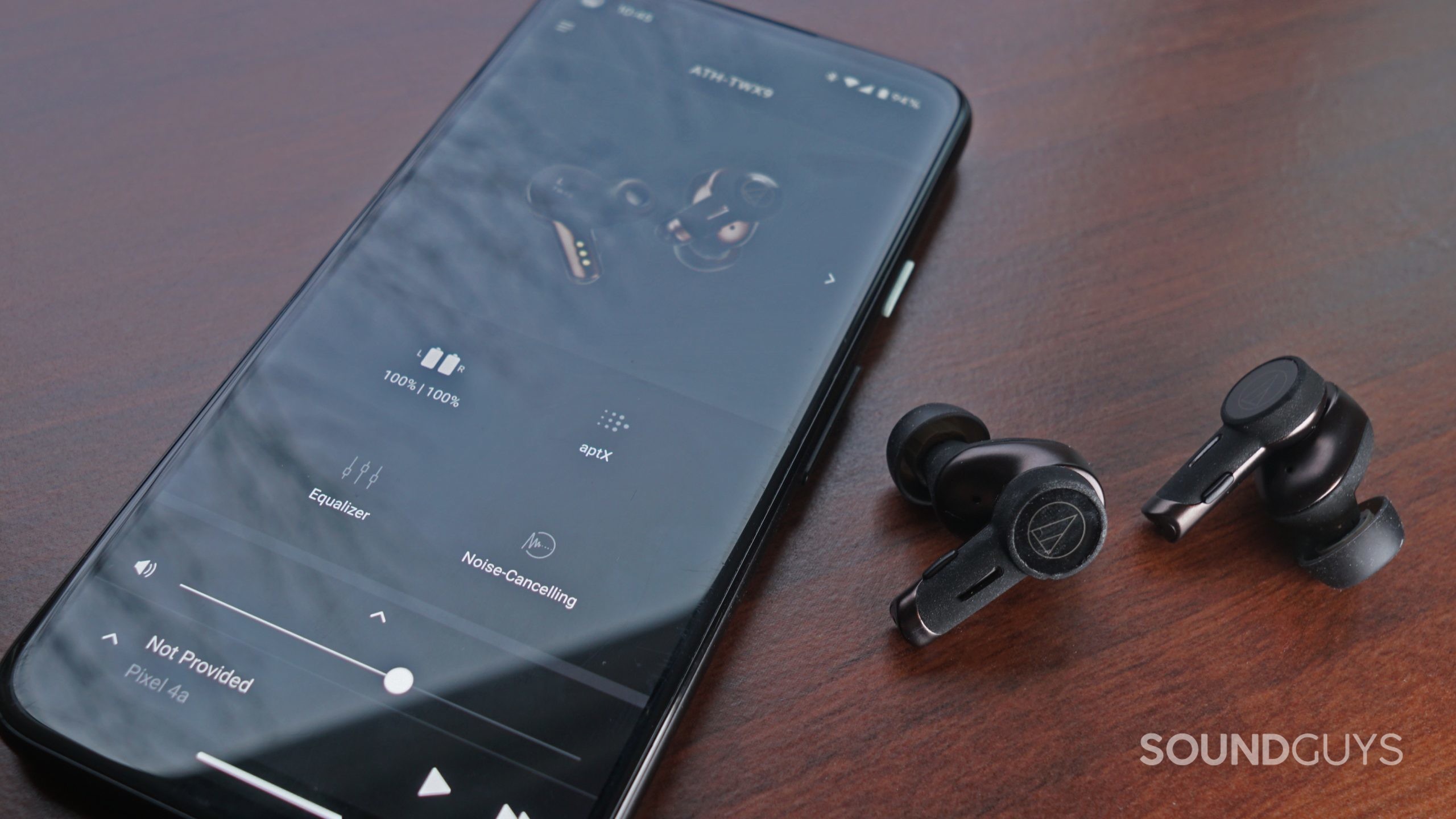 The Audio-Technica ATH-TWX9 earbuds lay on a wooden surface next to a Google Pixel 4a running the Audio-Technica Connect app.