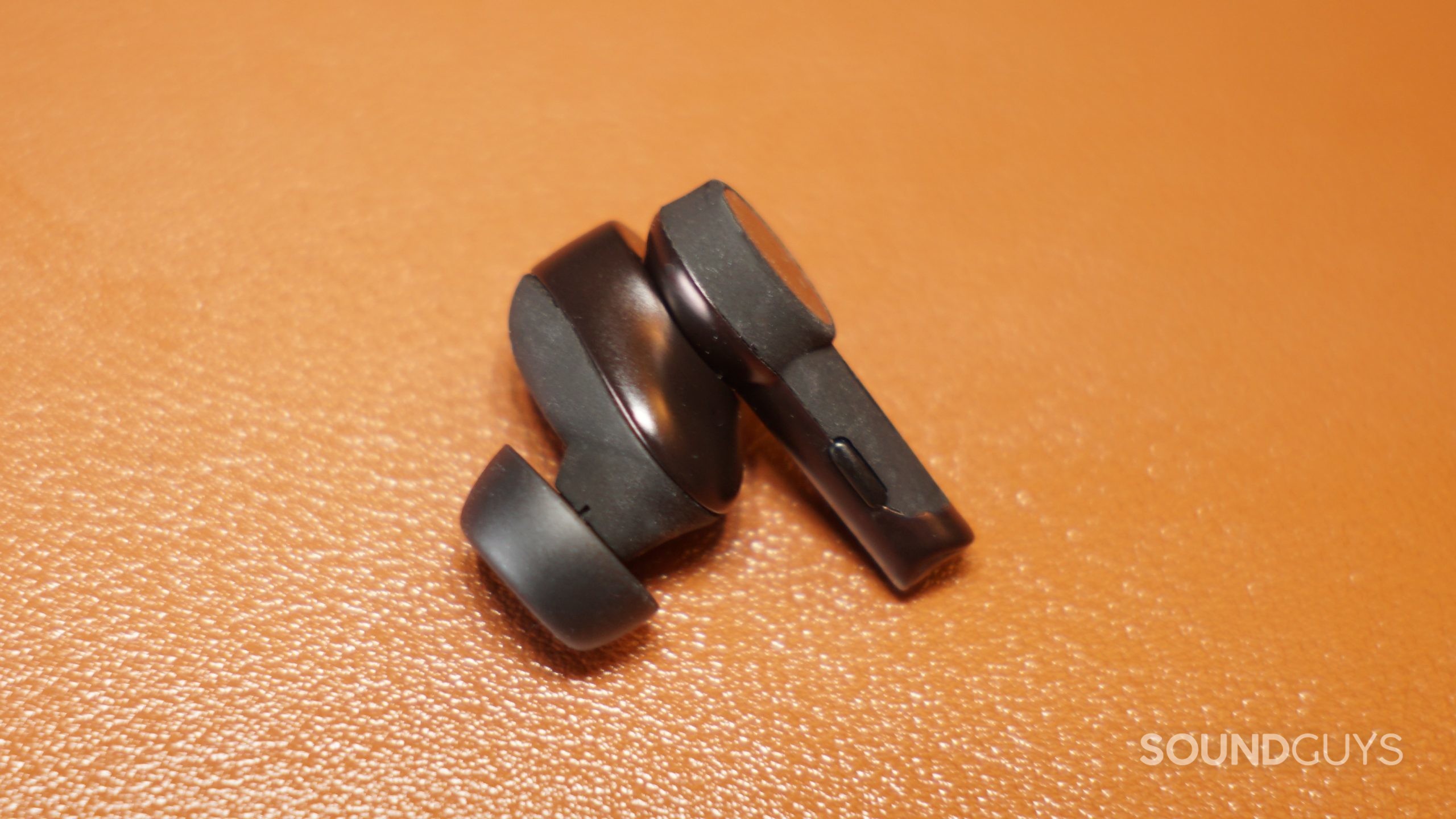 A single Audio-Technica ATH-TWX9 earbud lays on a leather surface.