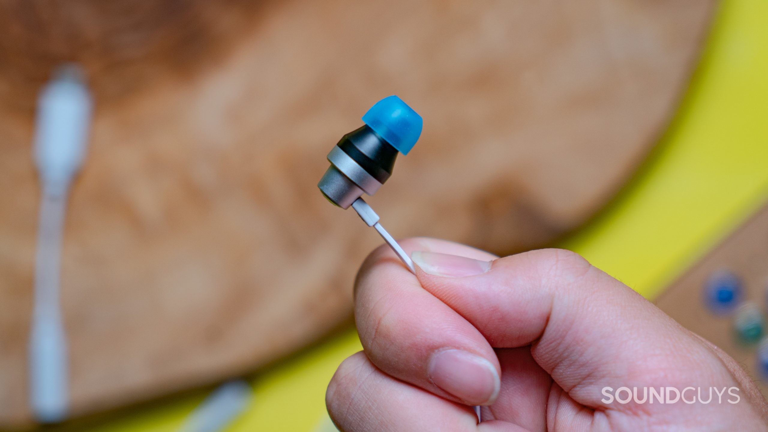 Someone holding one of the earbuds of the Logitech G333, showing the blue tip on black and silver aluminum housing.