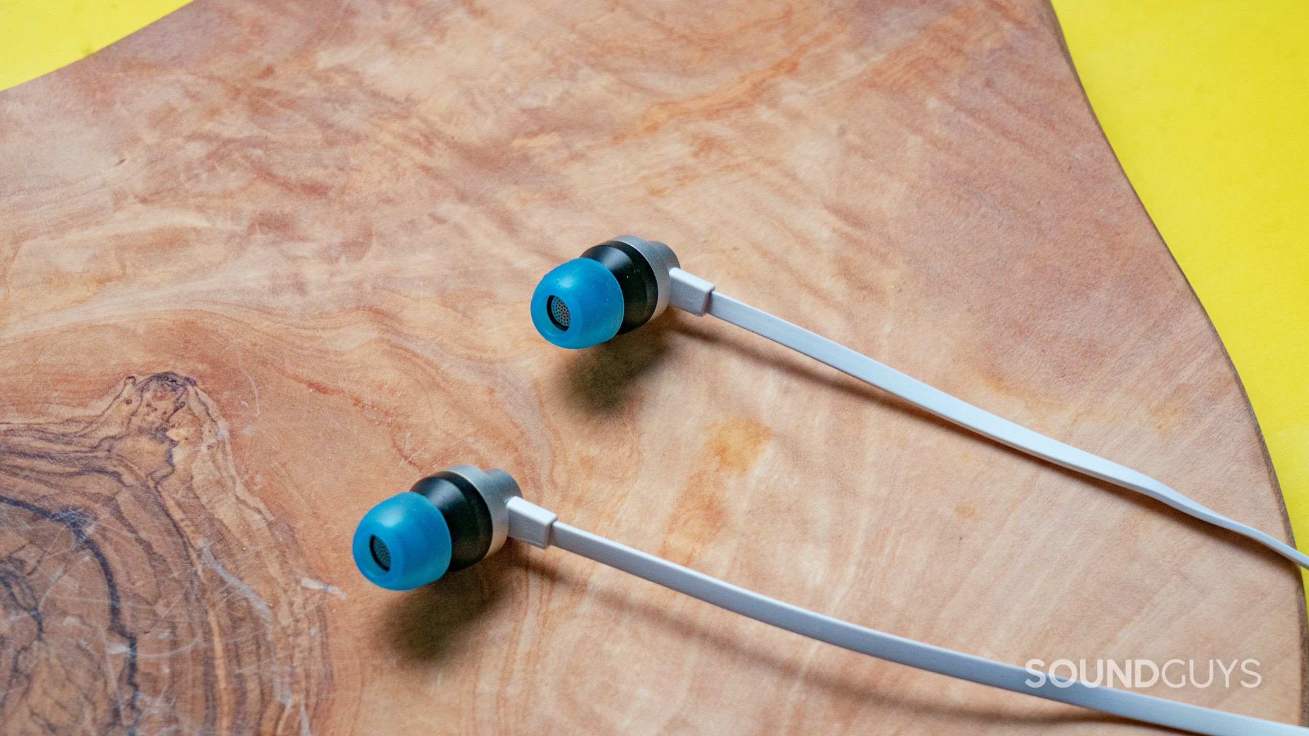 The two earbuds of the Logitech G333 sitting on a wooden table, facing neatly in the same direction.