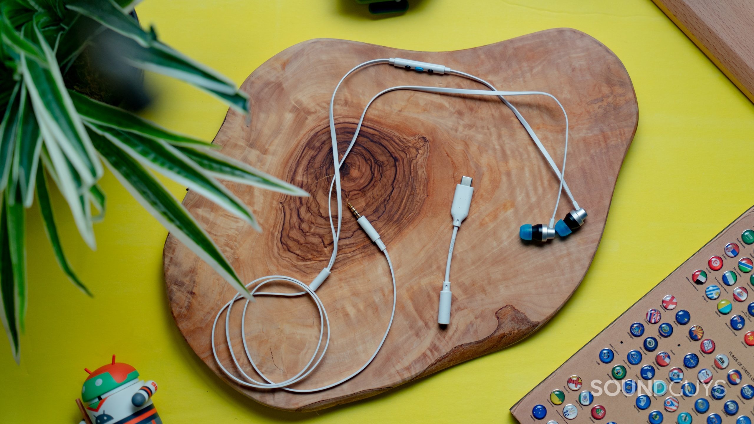The Logitech G333 earbuds and cable placed on top of a wooden surface with a plant to the left of them.