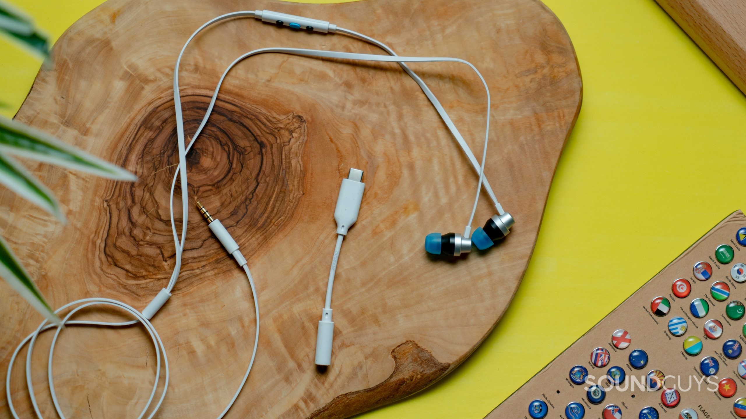 The Logitech G333 earbuds on a wooden surface, with the included USB-C to 3.5mm connector alongside them.