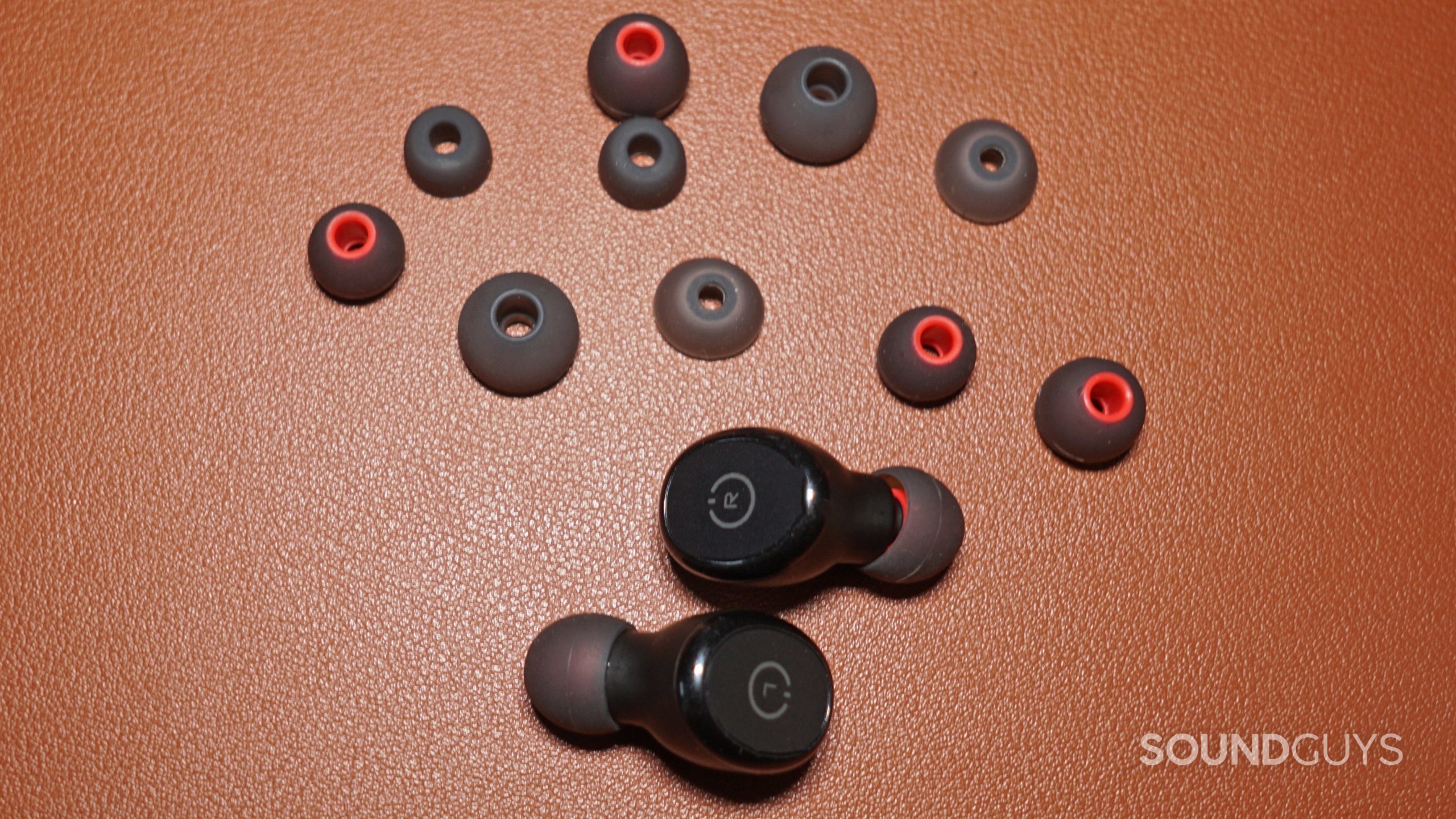 The TOZO T10 lays on a leather surface next to all its additional ear tips.
