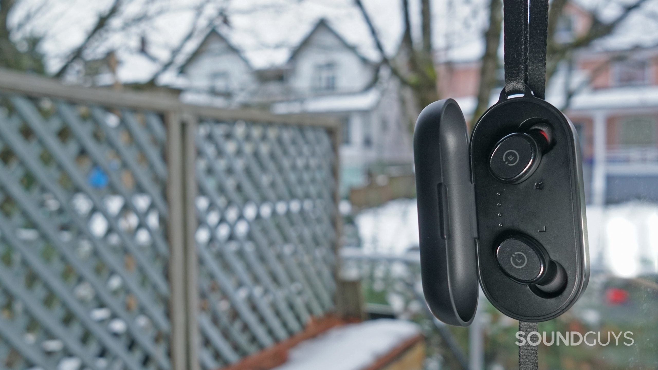 The TOZO T10 charing case hangs from its strap with the earbuds inside.