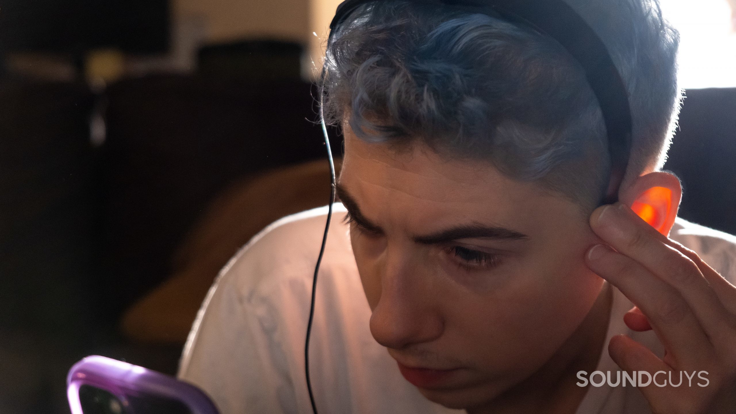 A man wears the headset for the Adaptiq function on the Bose Smart Soundbar 900, while holding a phone to activate the calibration.