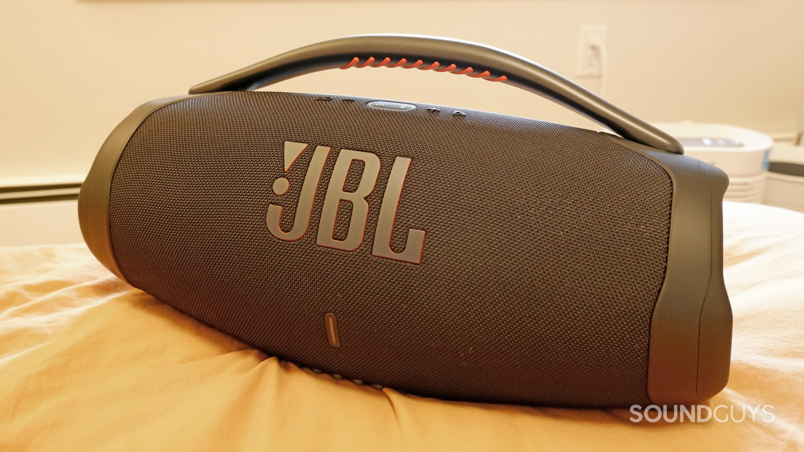The JBL Boombox 3 sitting on a bed with yellow sheets.
