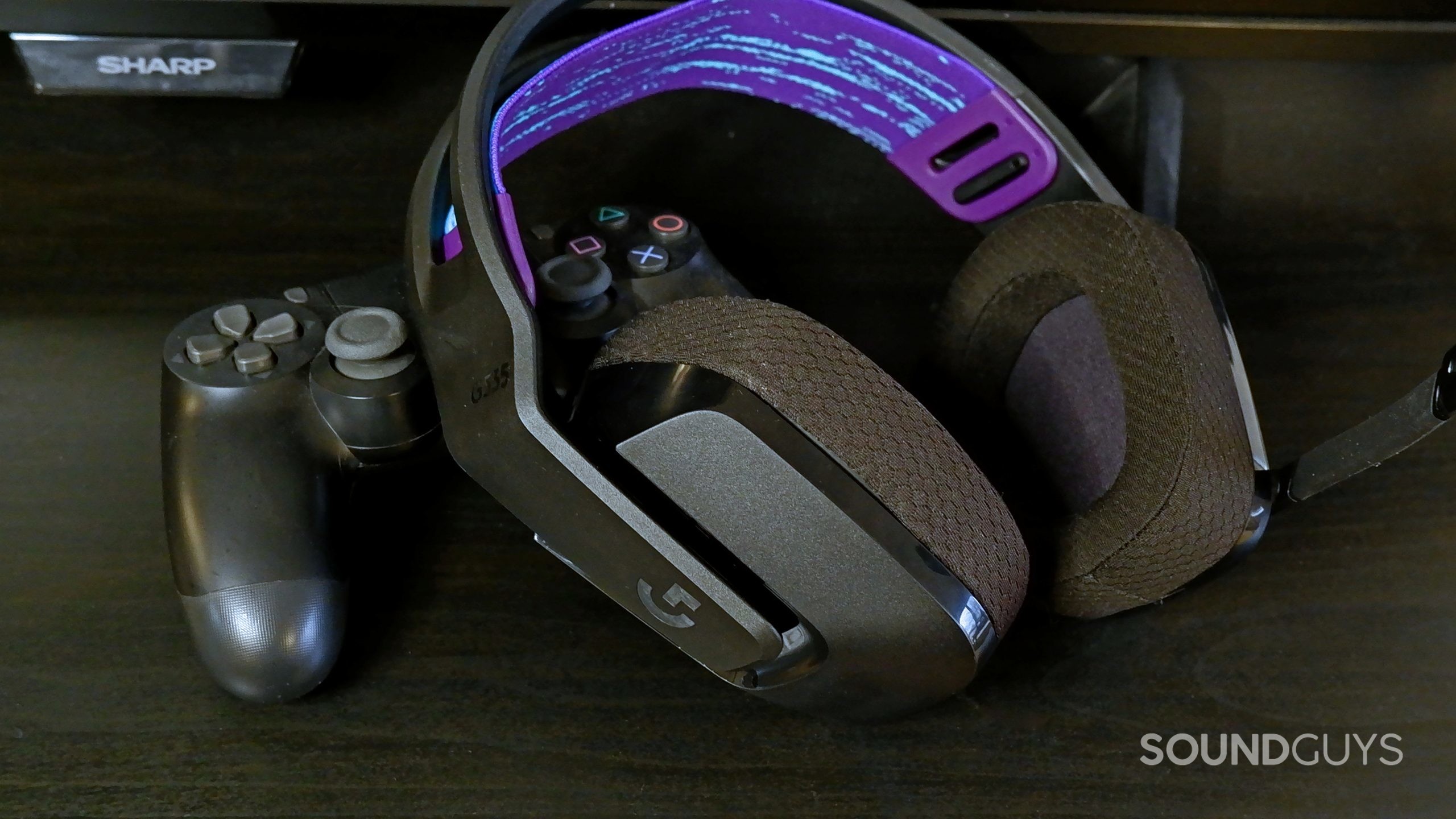 The Logitech G535 headset in front of a TV, resting on a PlayStation 4 controller.