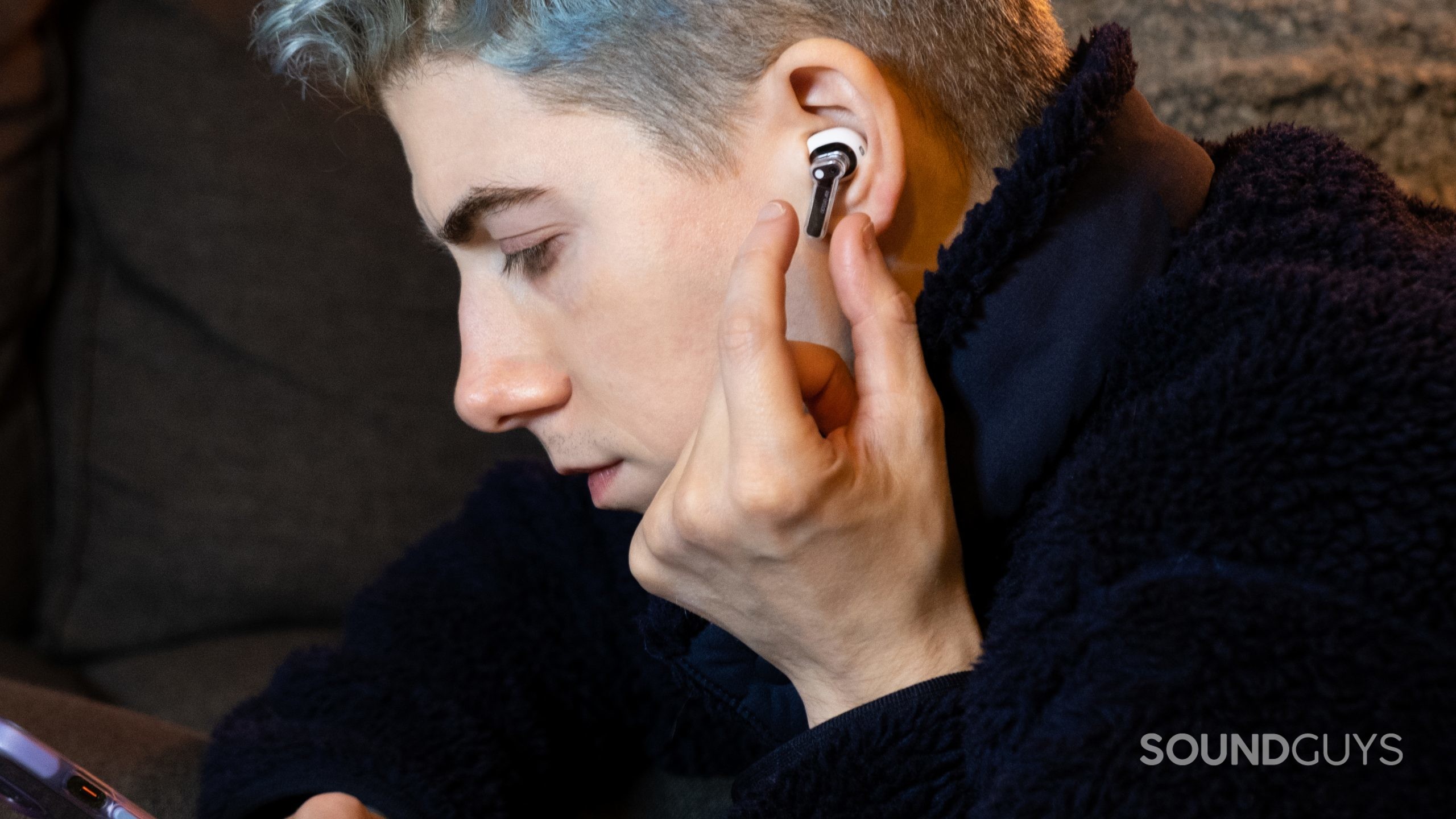 A man faces left holding a phone and about to pinch the Nothing Ear (stick).