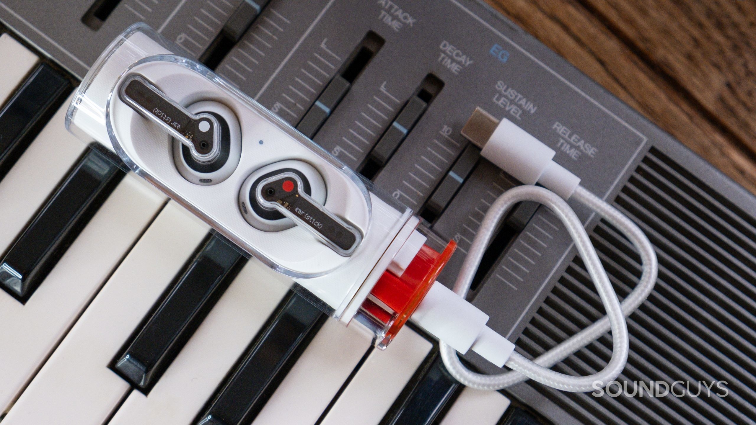The open case of the Nothing Ear stick with the included USB-C to USB-C cable rests atop a grey analog synth.