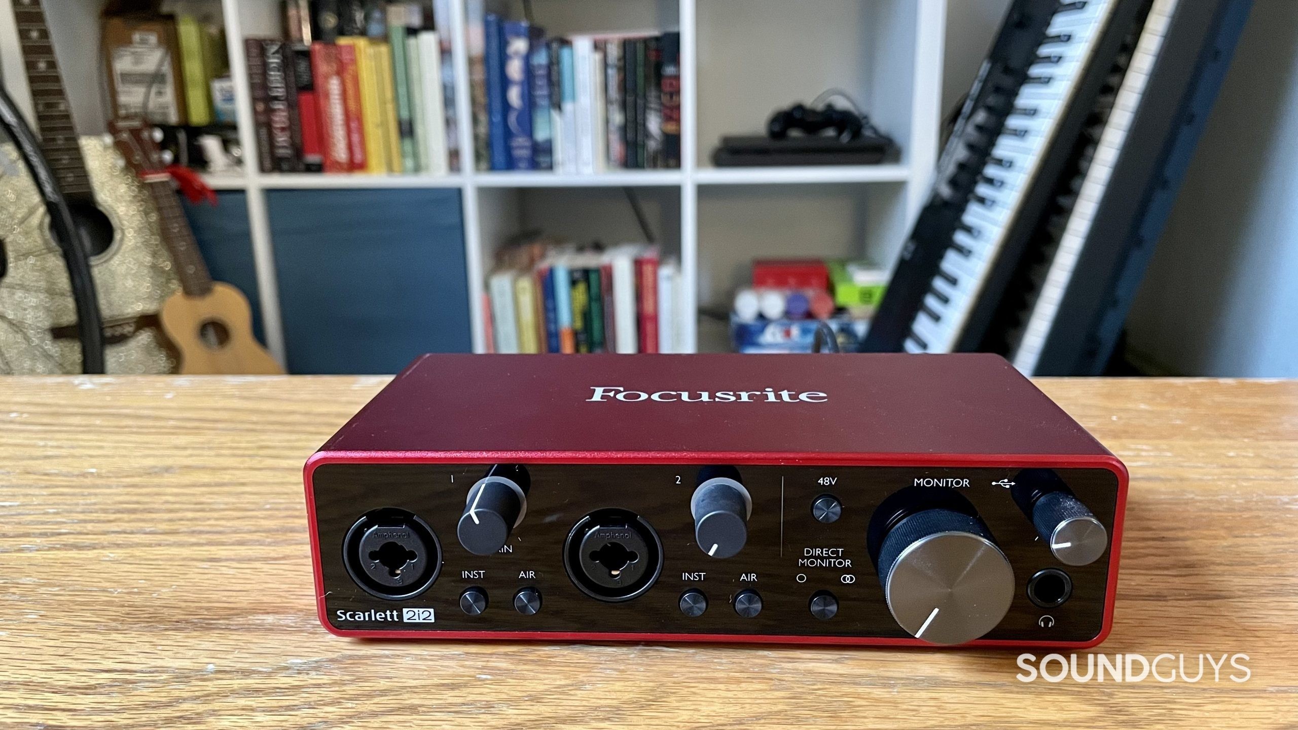 Focusrite Scarlett 2i2 on a table with a bookshelf and instruments in the background.