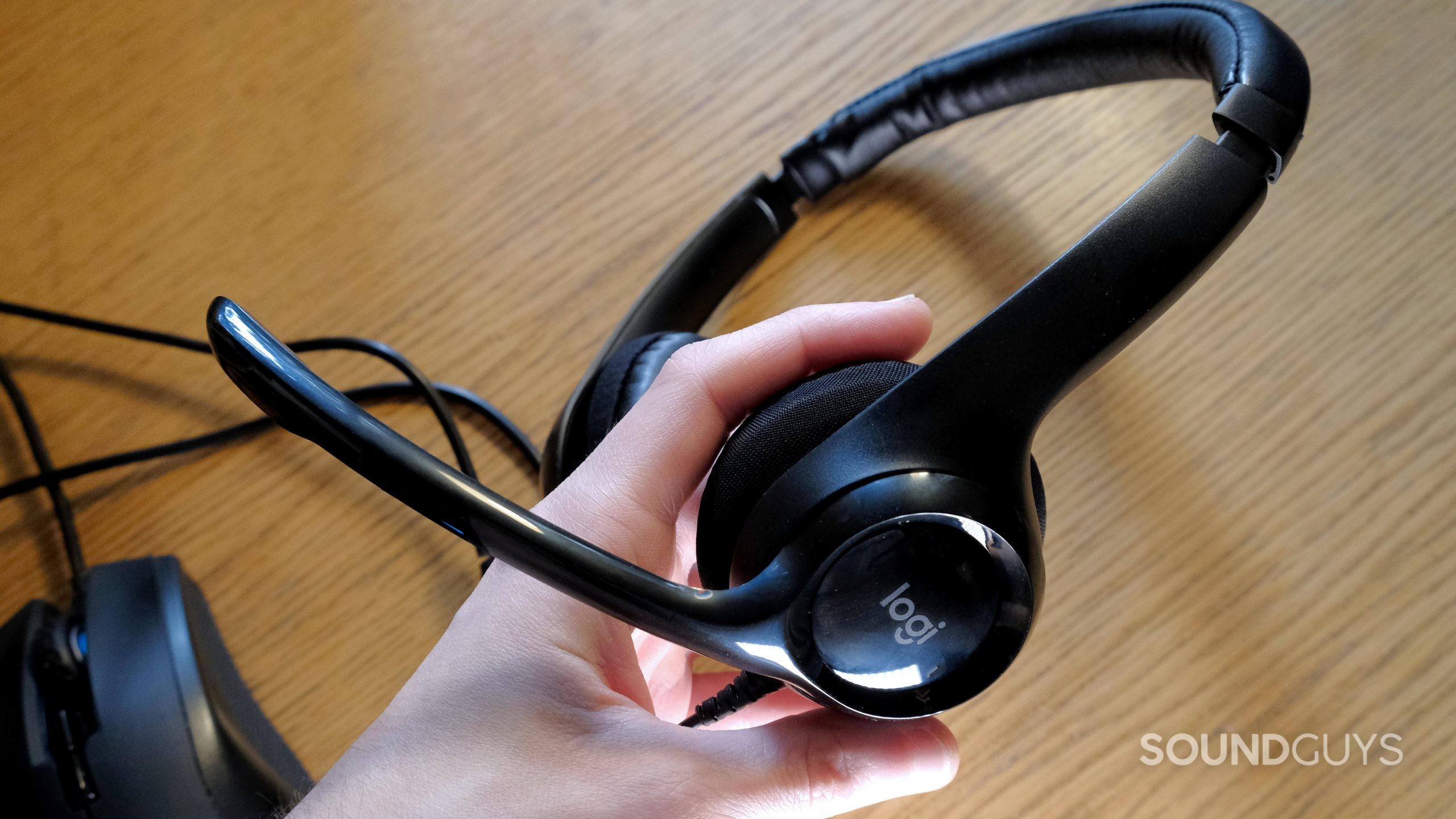 A hand holds the Logitech H390 from the side above a wood surface.