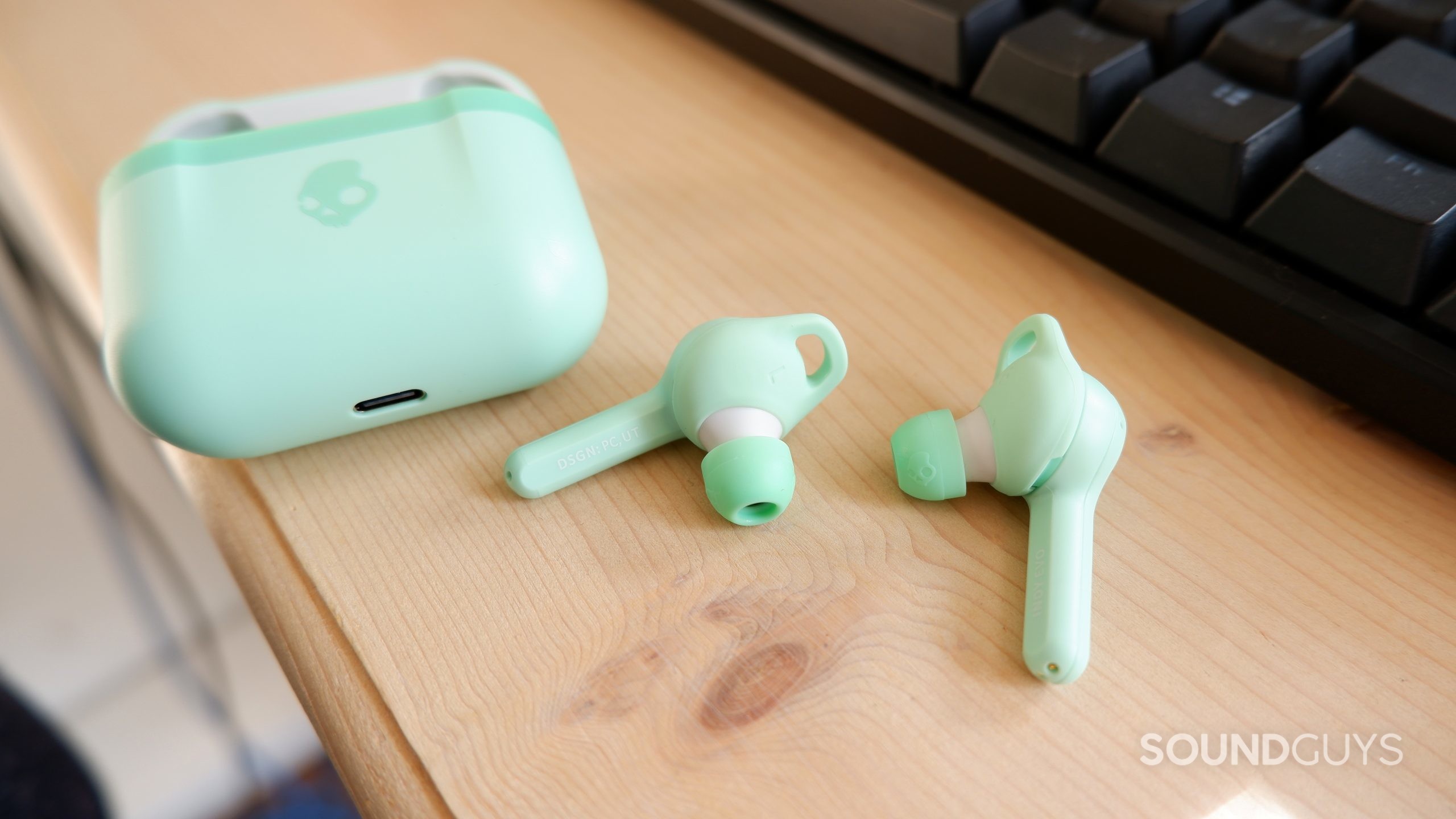 The Skullcandy Indy Evo earbuds on a wooden desk next to the case.