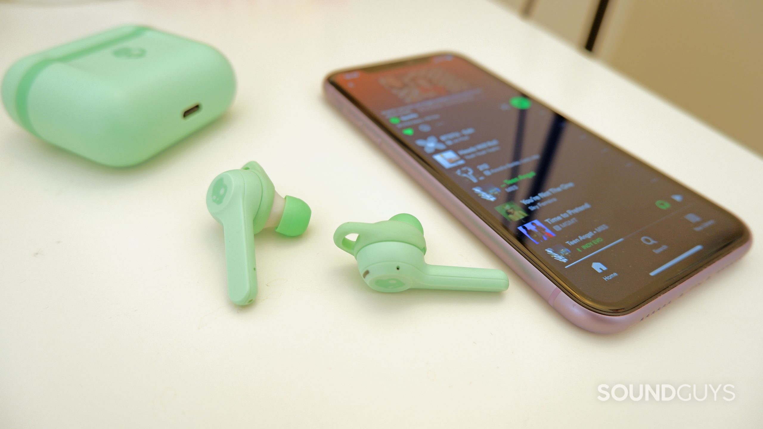 The Skullcandy Indy Evo on a table beside a phone with Spotify open.