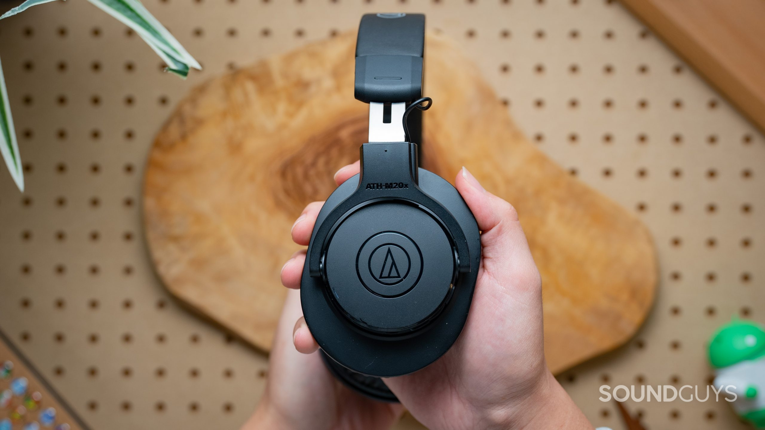 A photo of the closed backs of the Audio-Technica ATH-M20XBT headphones, set in front of pegboard and wood.