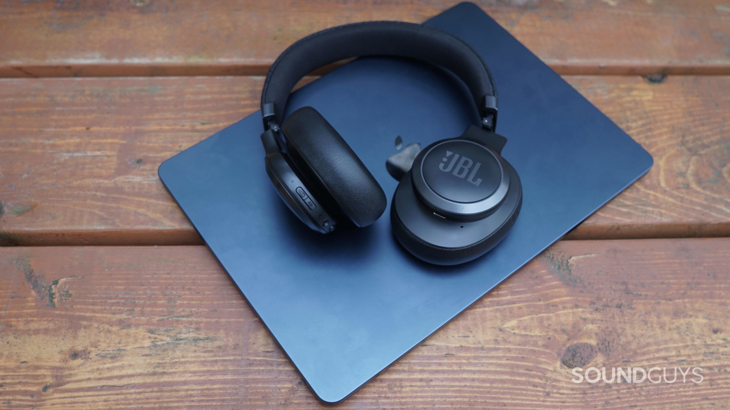The JBL Tune 600NC lays on an Apple MacBook Air sitting on a wooden surface.