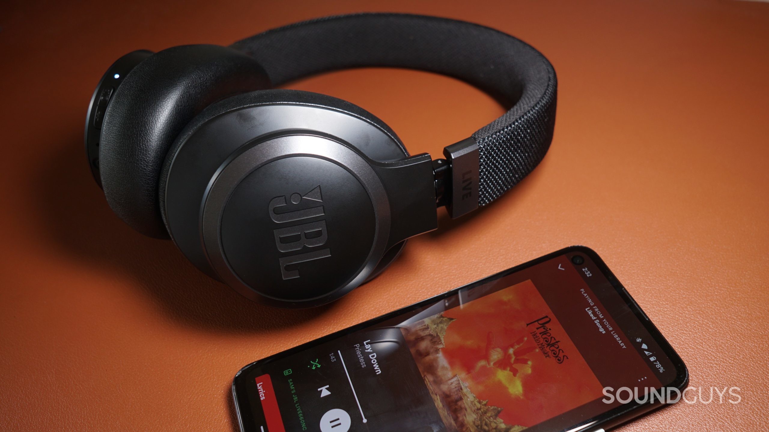 The JBL Live 660NC lays on a leather surface next to a Google Pixel 4a running Spotify.