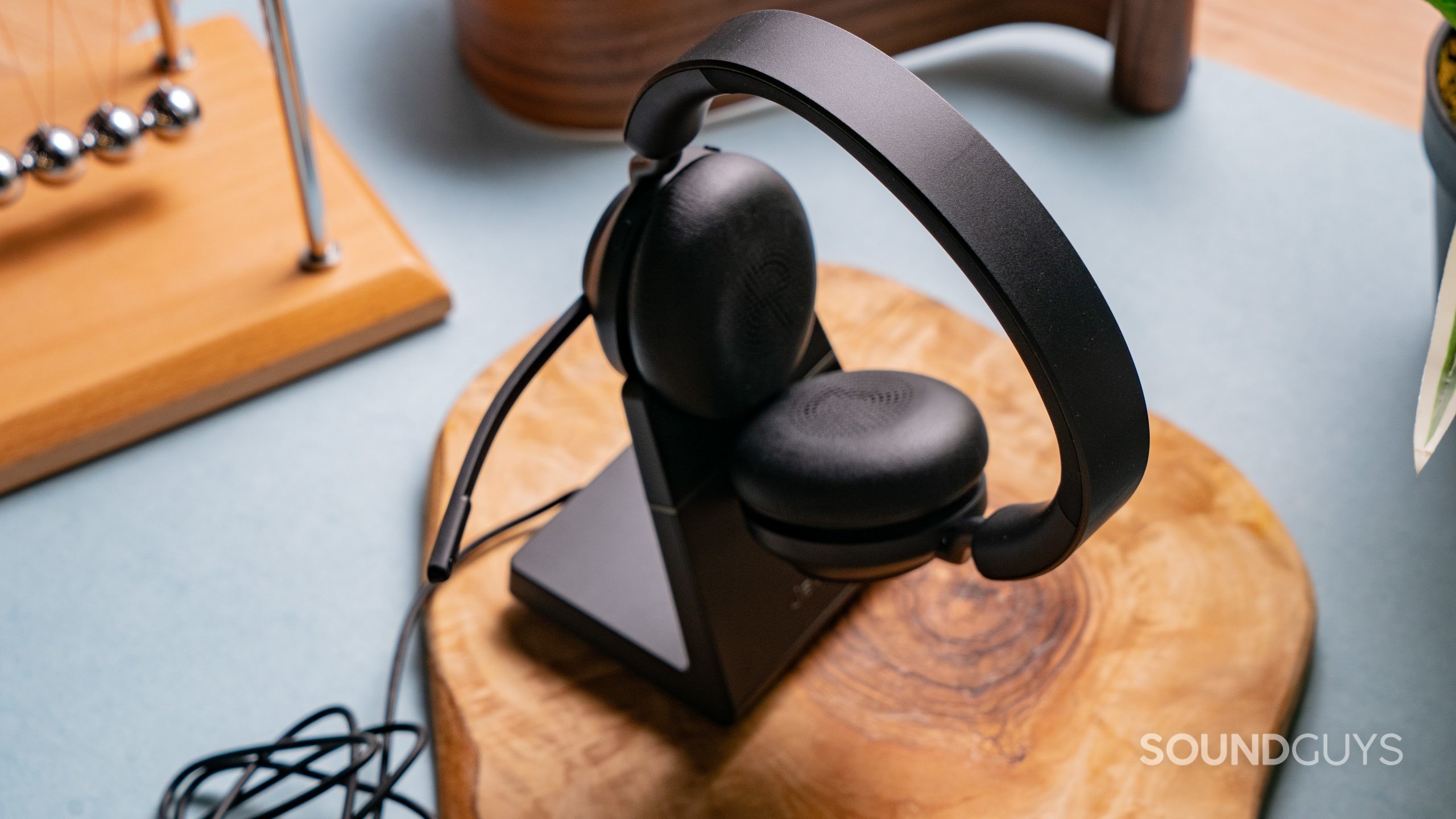The Jabra Evolve2 65 sitting in its charging cable on top of a wooden surface.