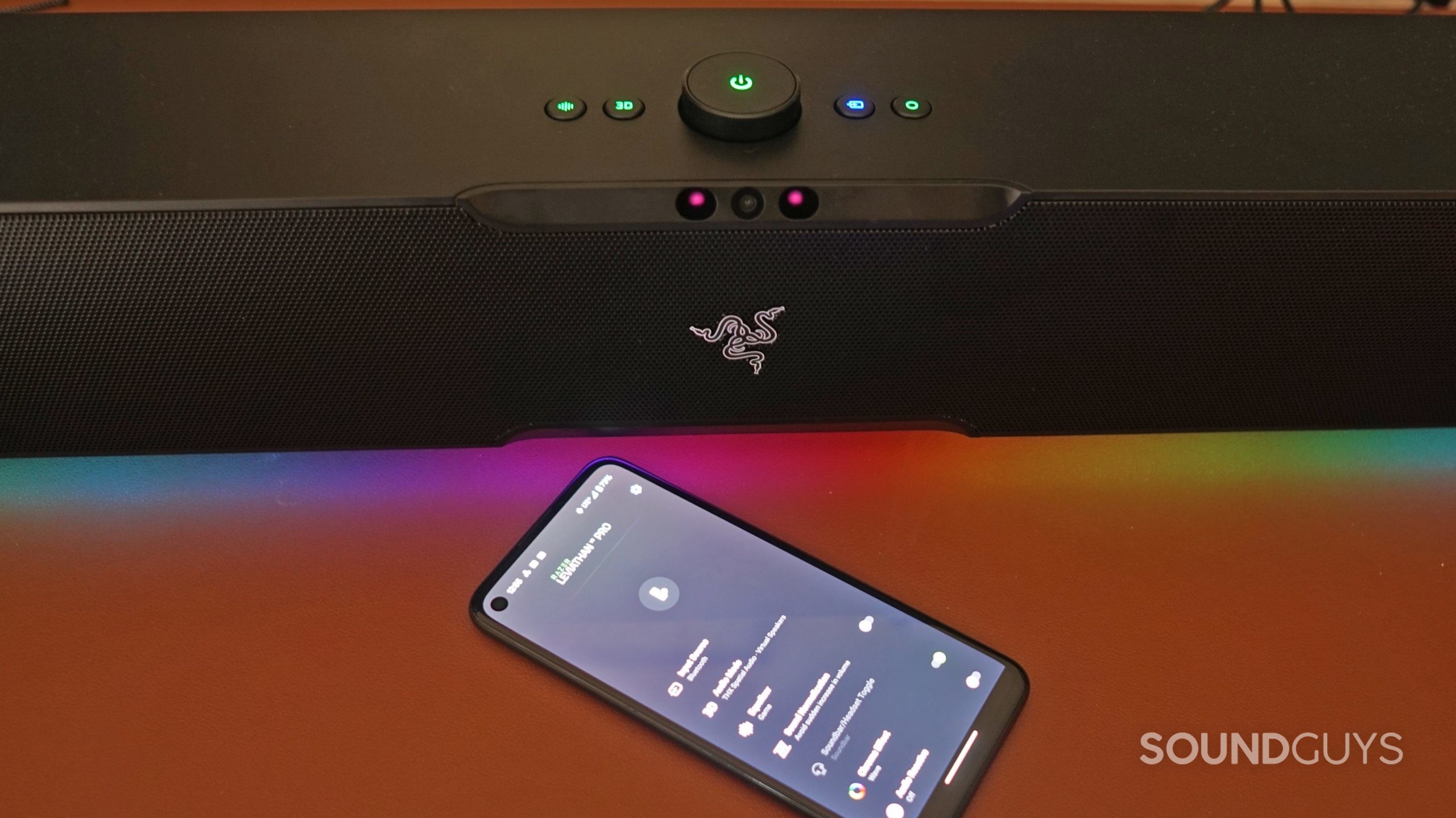 The Razer Leviathan V2 Pro sits on a leather surface, next to a Google Pixel 4a running the Razer Audio app.