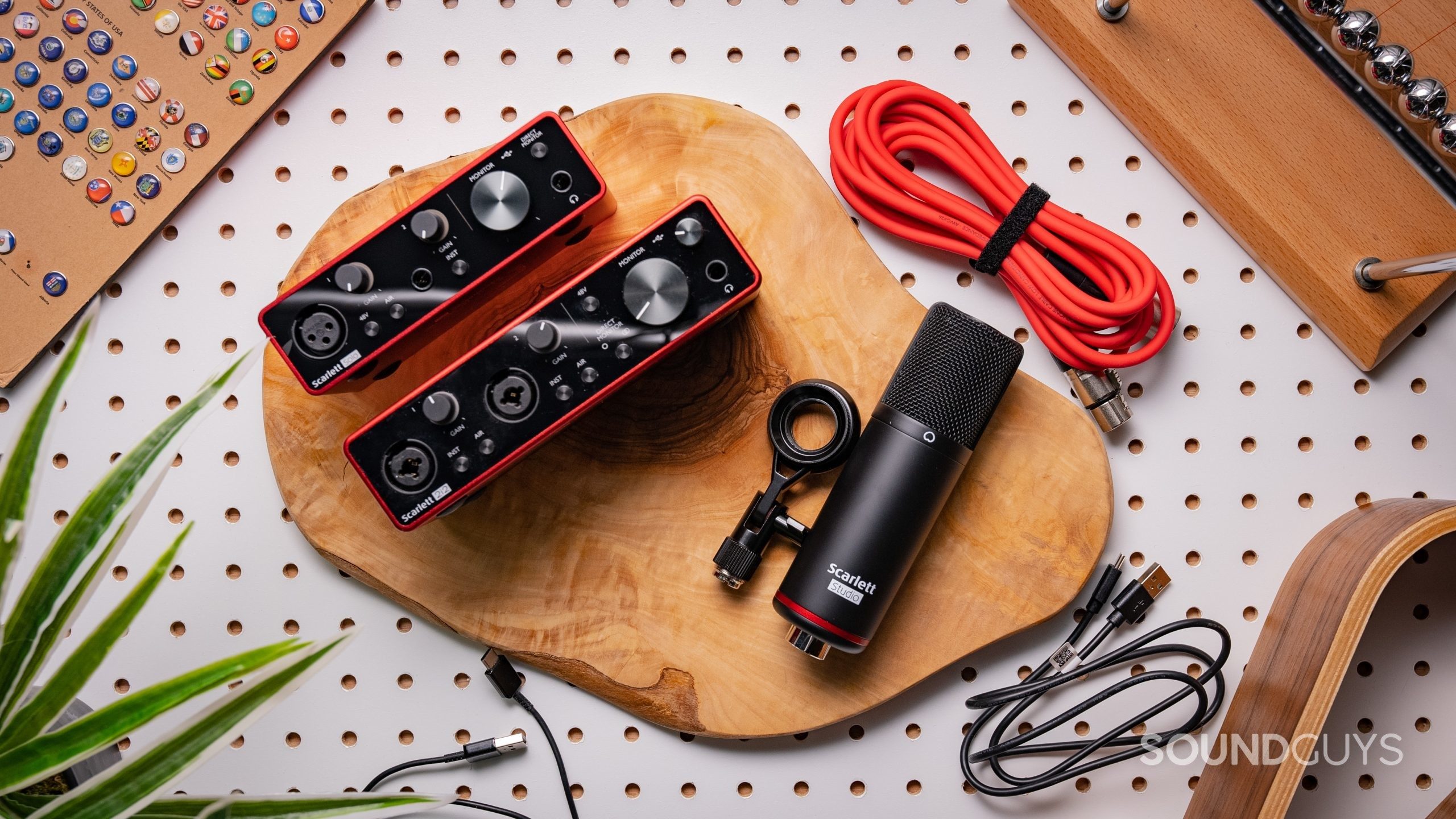 Focusrite Scarlett 2i2 and Scarlett Solo interfaces, CM25 MkIII condenser microphone, and some cables resting on a peg board.