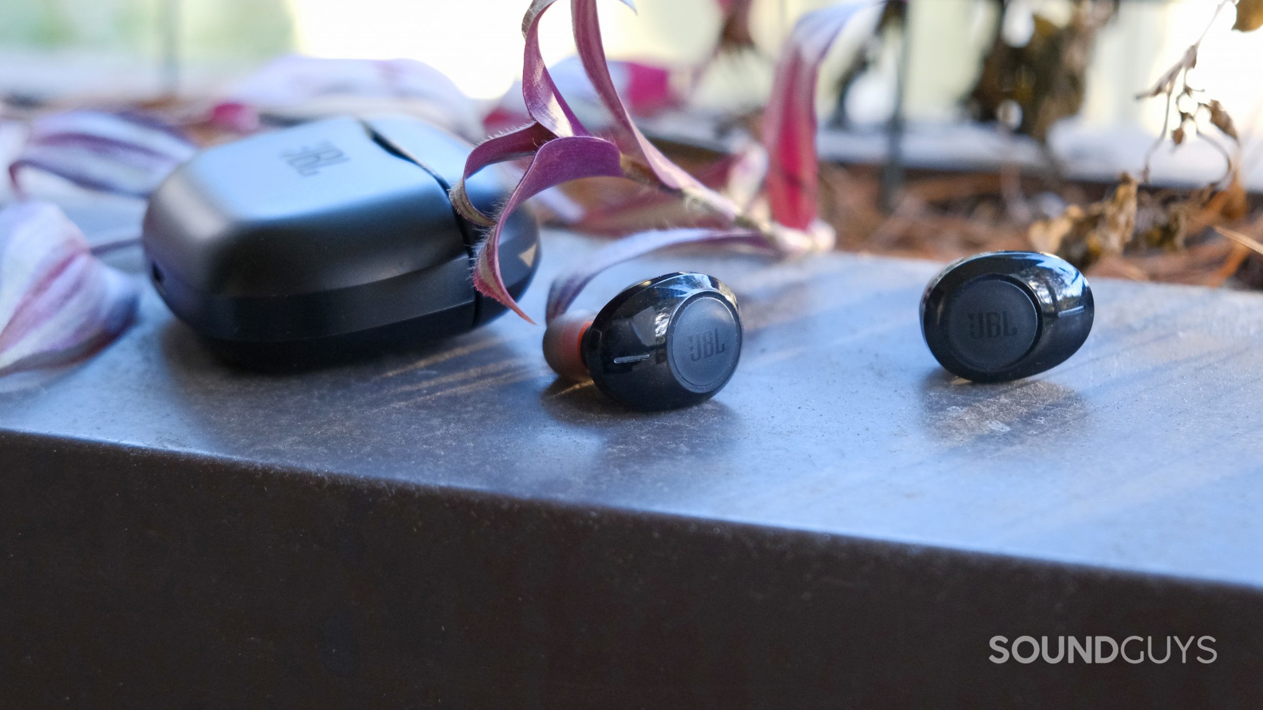 The JBL Tune 125TWS earbuds rest on a ledge with the case.