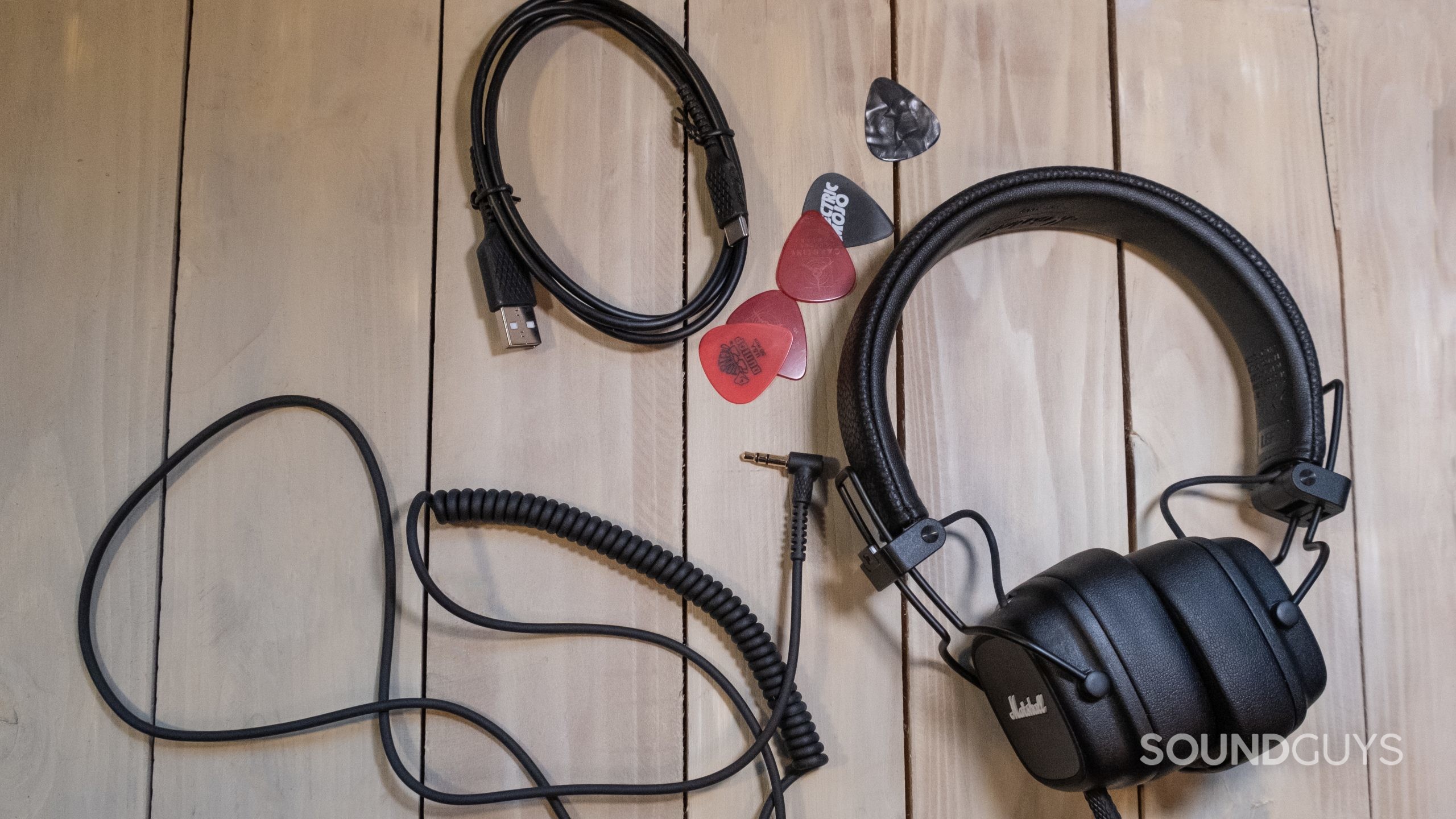 On a light wood surface are the cables and Marshall Major IV headphones.