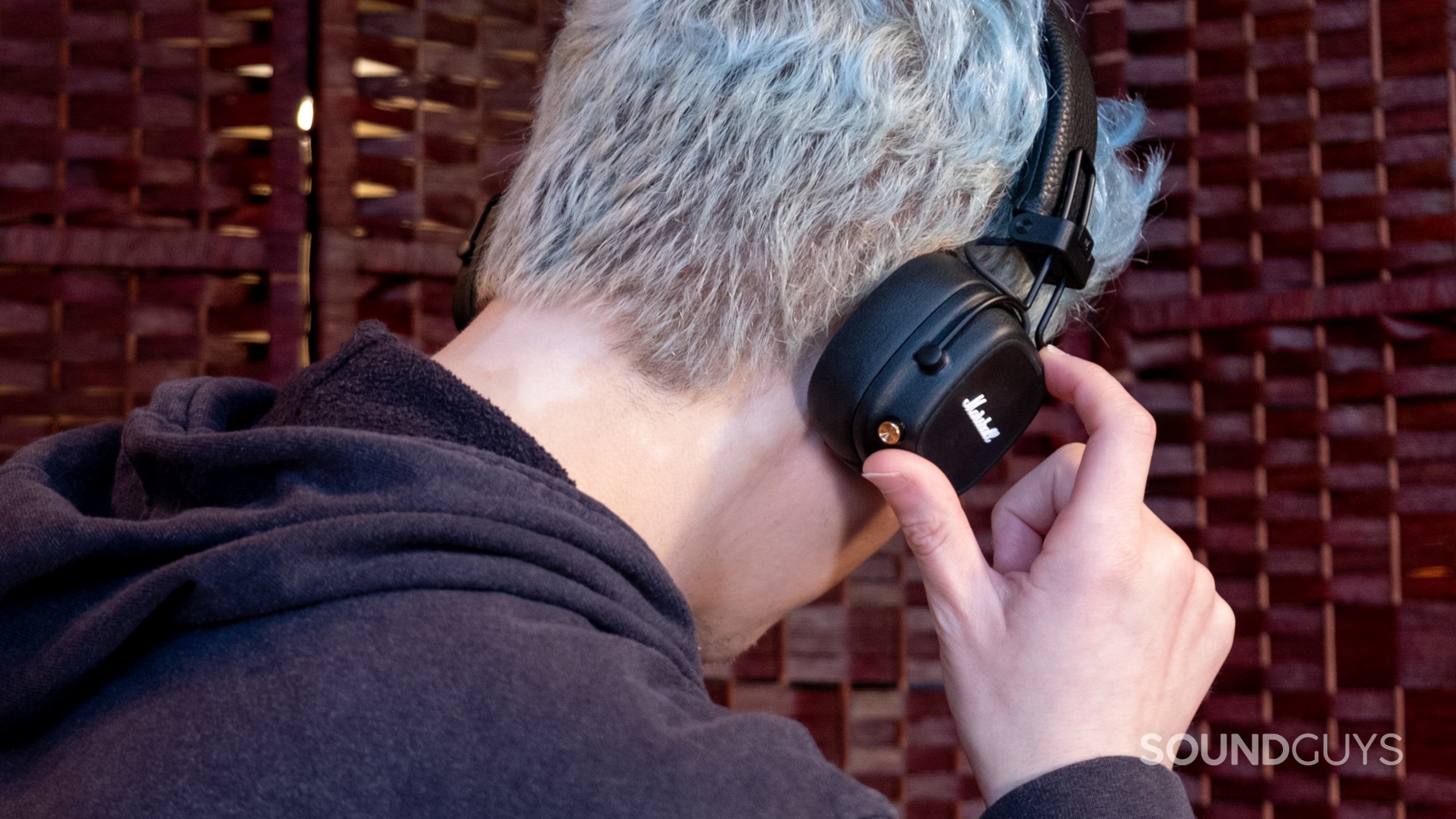 A man faces away from the viewer with his right hand using the control on the Marshall Major IV.