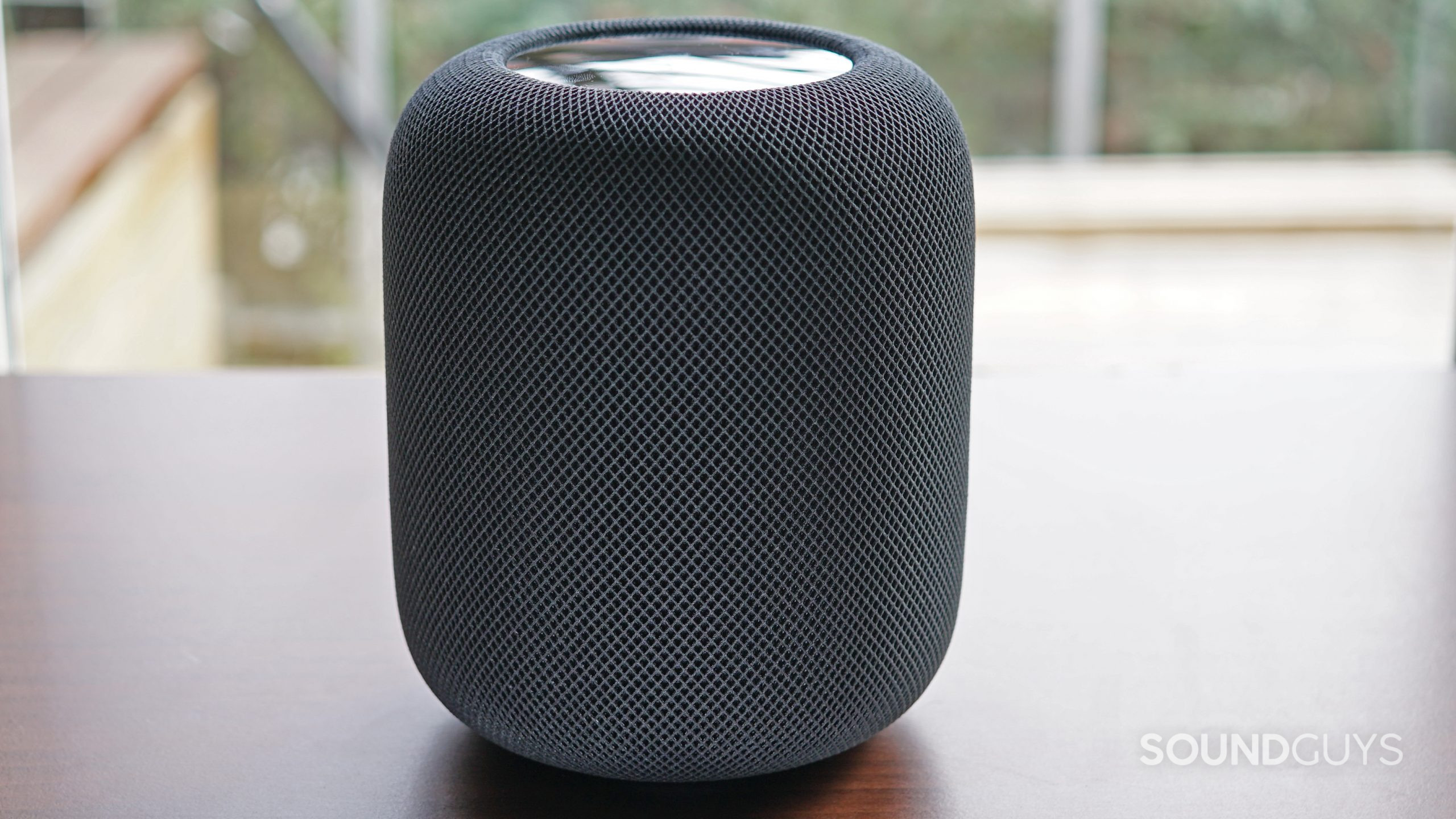 The Apple HomePod (2nd Generation) sits on a wooden shelf near a window.