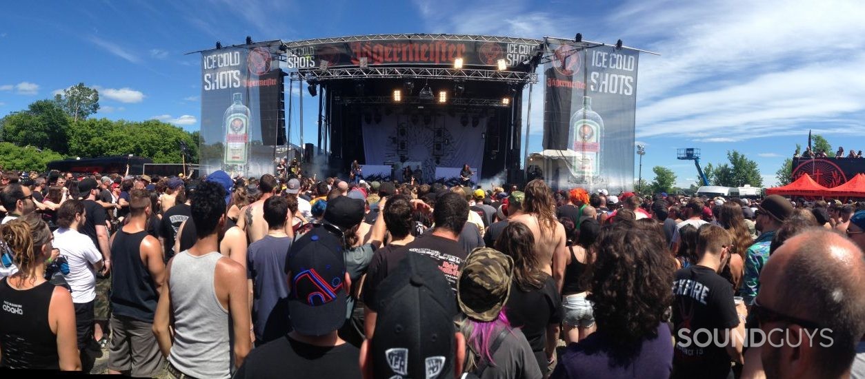 A crowd is gathered in front of an open air stage at a music festival