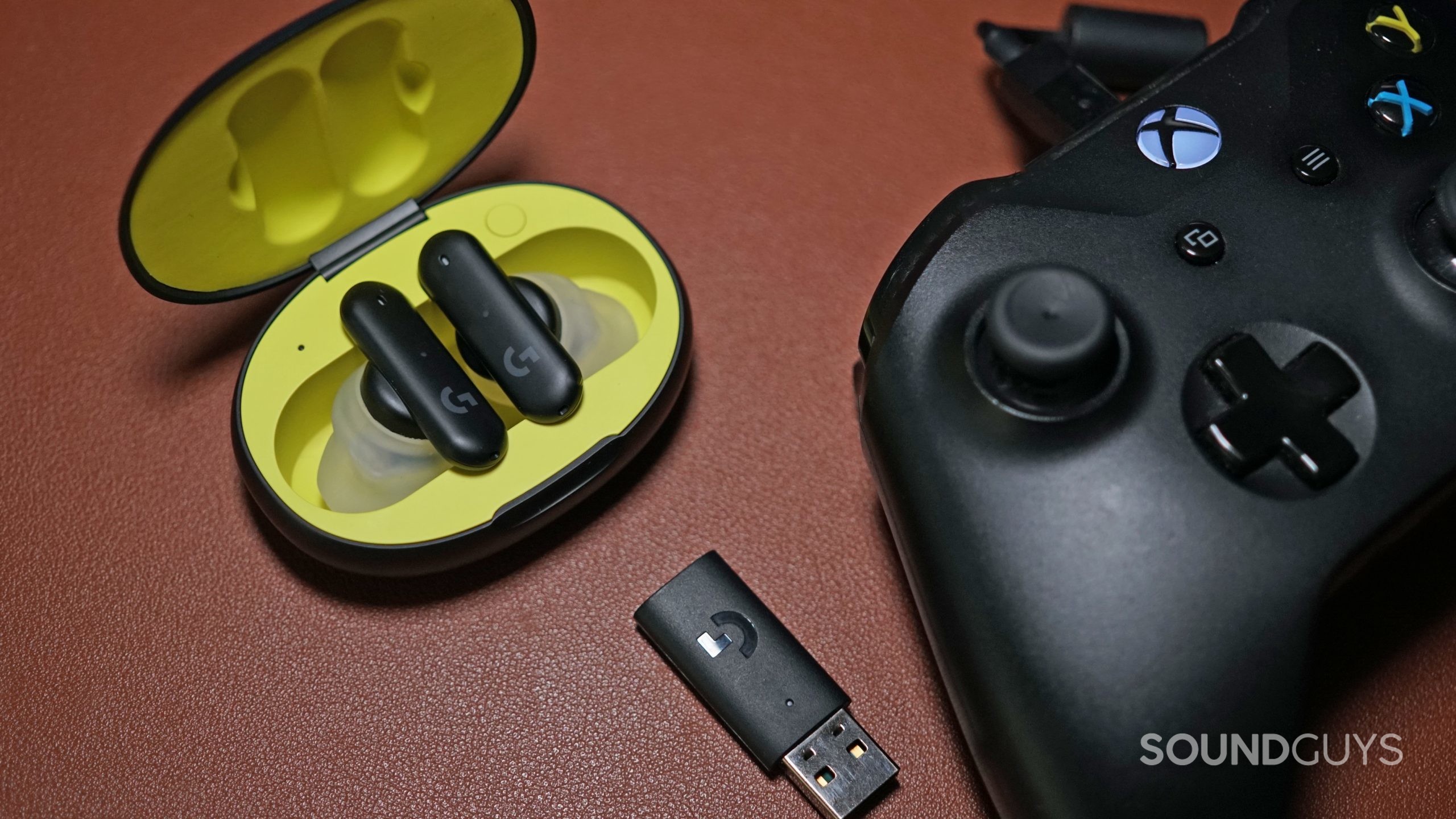 The Logitech G Fits earbuds sit in its charging case next to its USB dongle and an Xbox One controller.