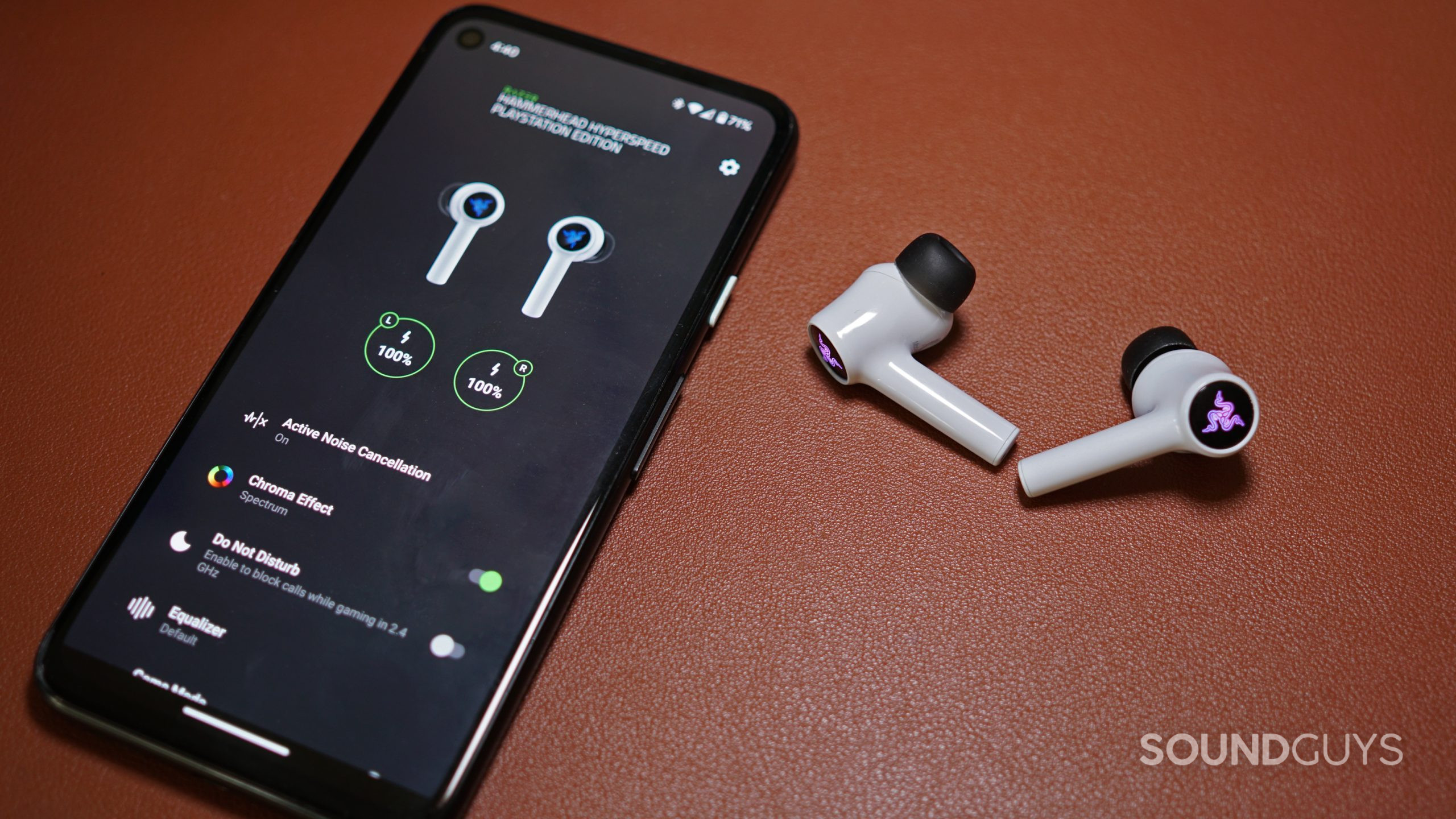 Photo of a Google Pixel 4a running the Razer Audio App laying on a leather surface next to the Razer Hammerhead Hyperspeed earbuds.