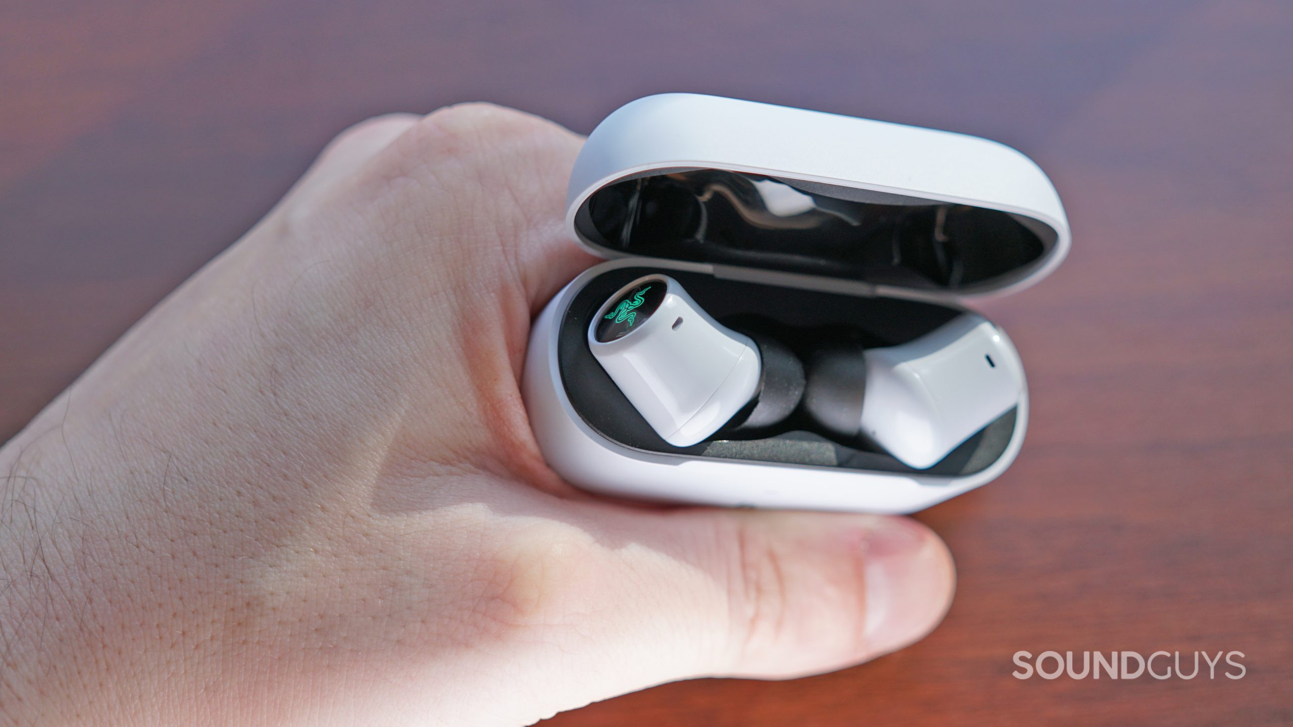 The Razer Hammerhead Hyperspeed earbuds sit in their charging case, being held by a hand.