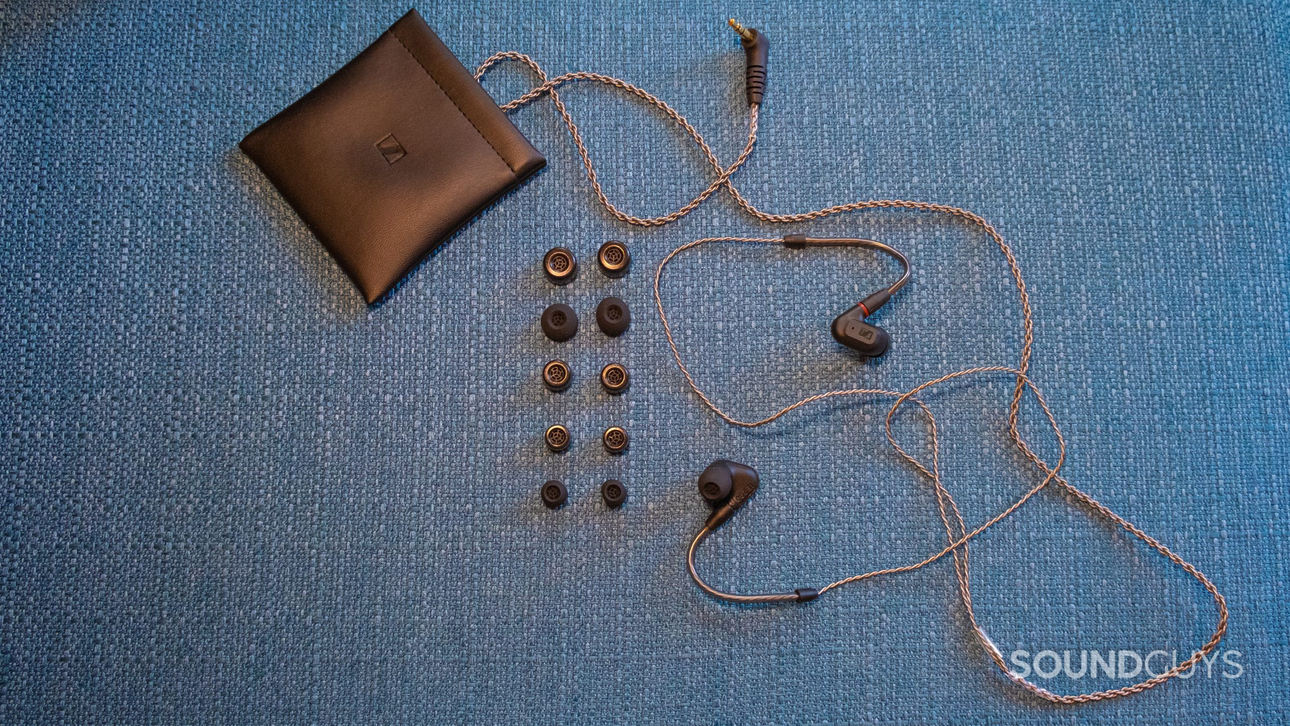 On a teal fabric bench surface the Sennheiser IE 200 is shown with its ear tips and pouch.
