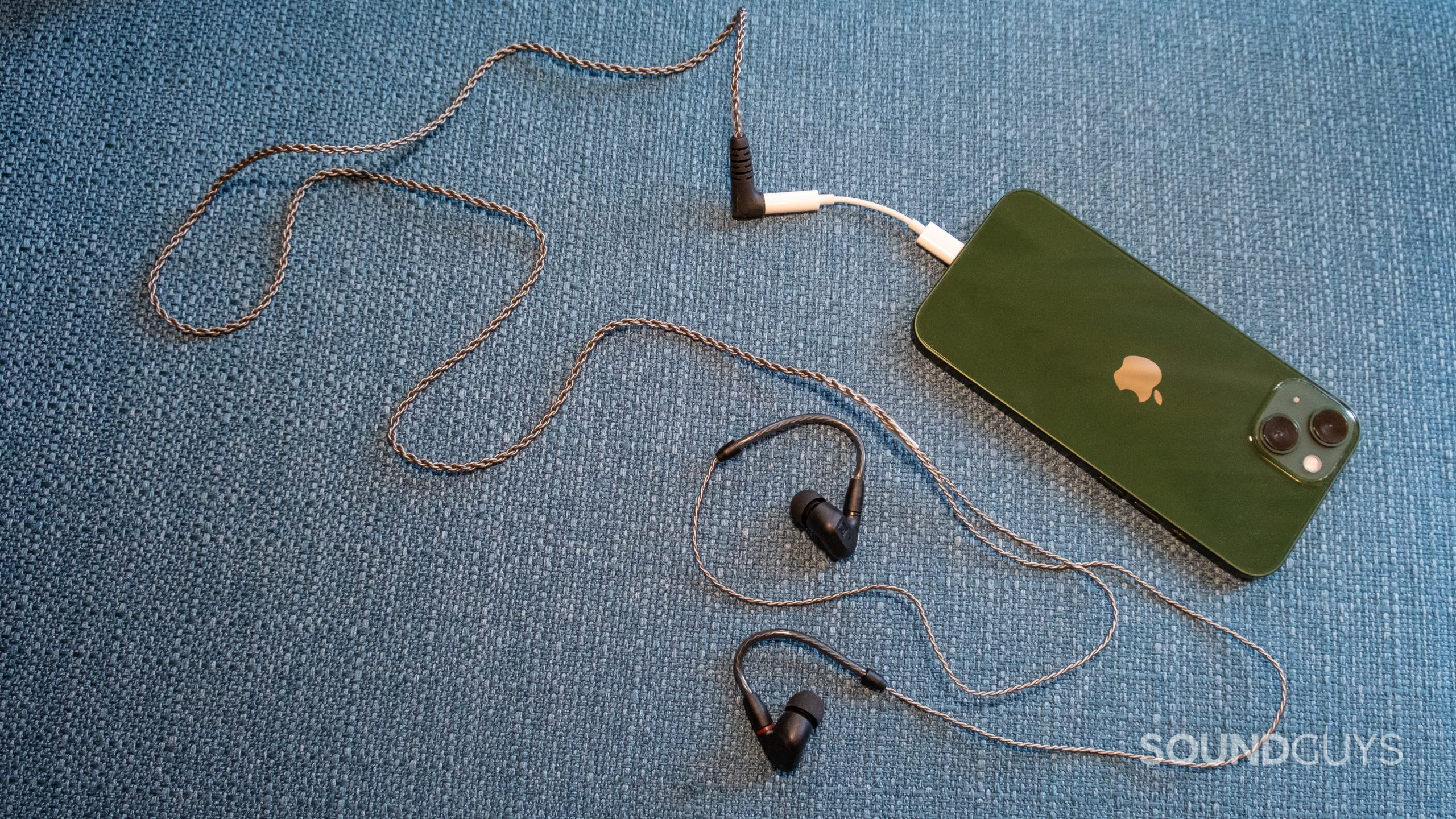 On a teal fabric surface the Sennheiser IE 200 is plugged into an Apple iPhone via a dongle.