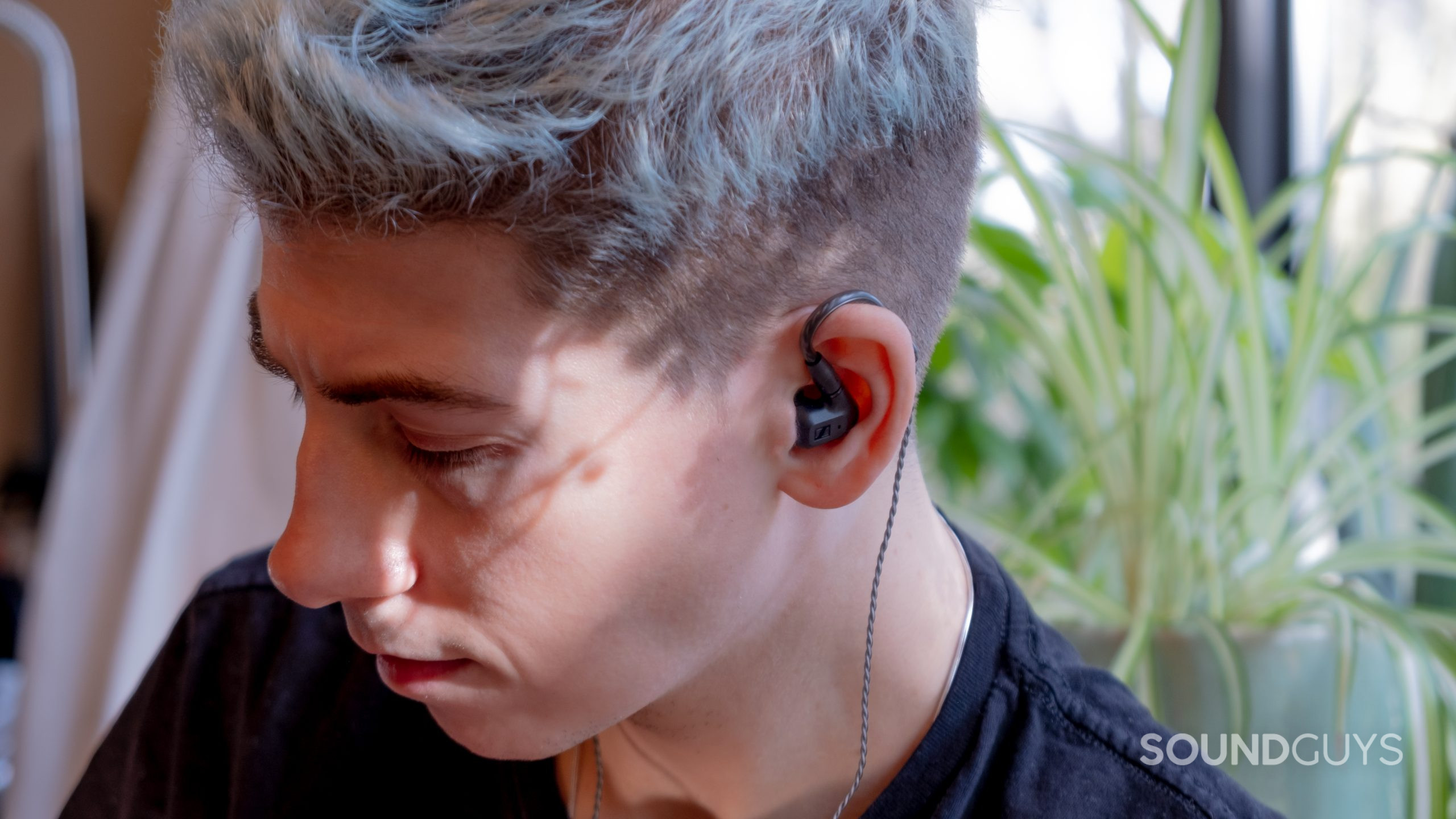 A man wears the Sennheiser IE 200 in ears with an aloe plant in the background.