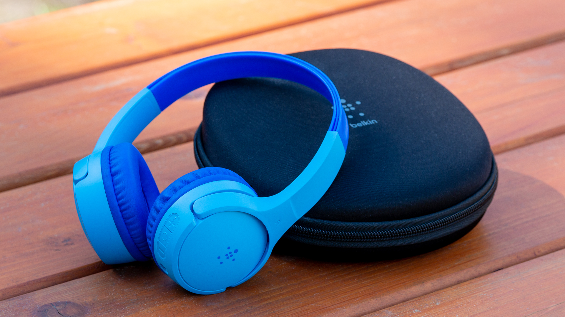 A photo of the Belkin SoundForm Mini sitting atop its case on a cedar bench.