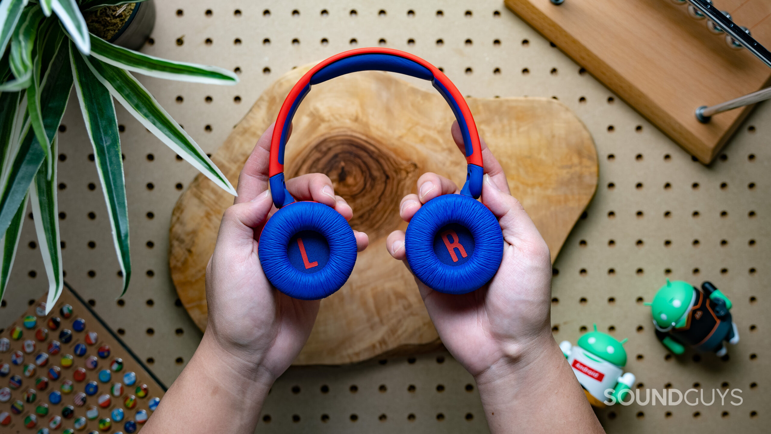 A photo of the JBL JR310BT being held in front of a pegboard desk.