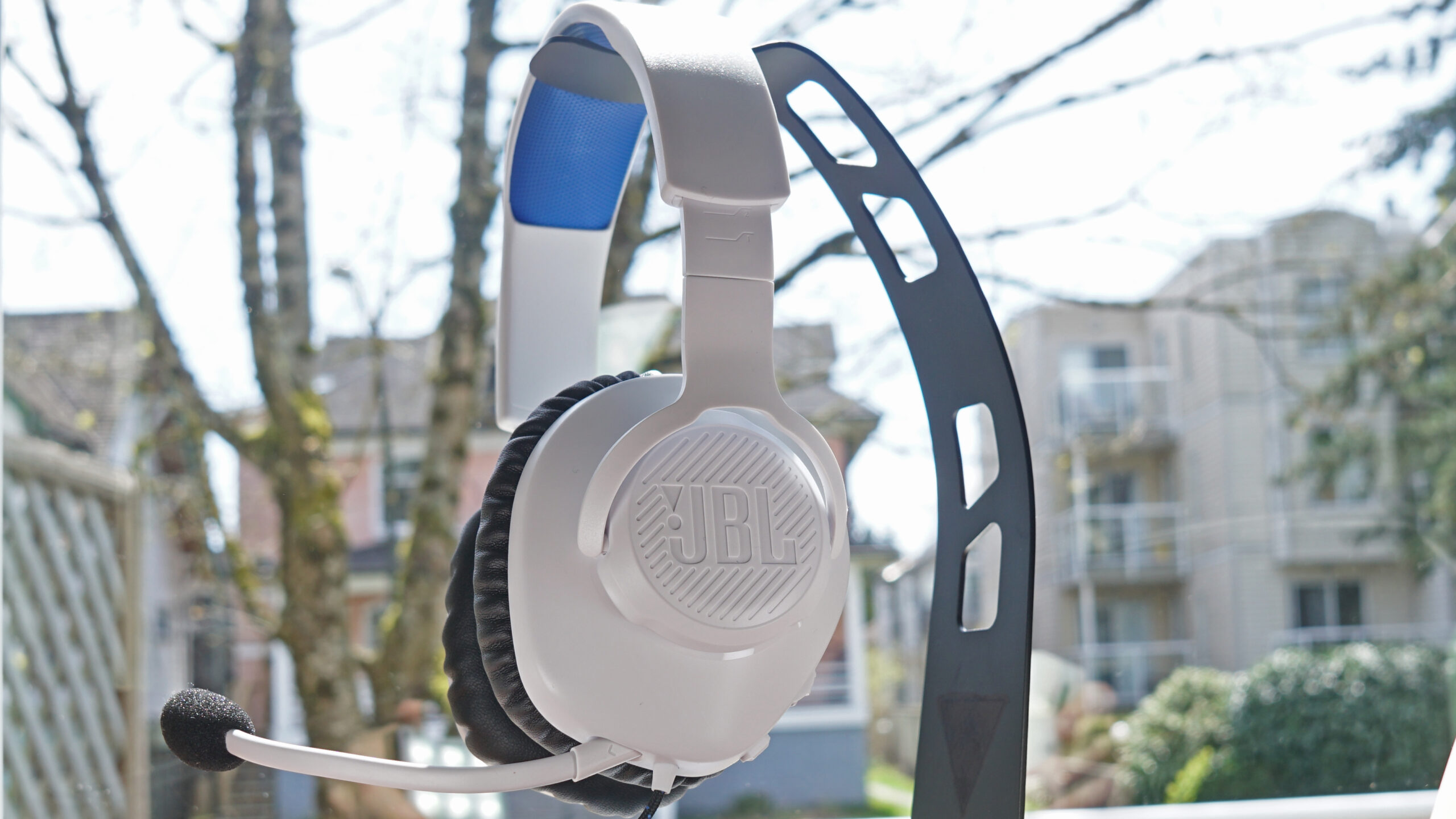 The JBL Quantum 100P gaming headset sits on a stand in front of a window.