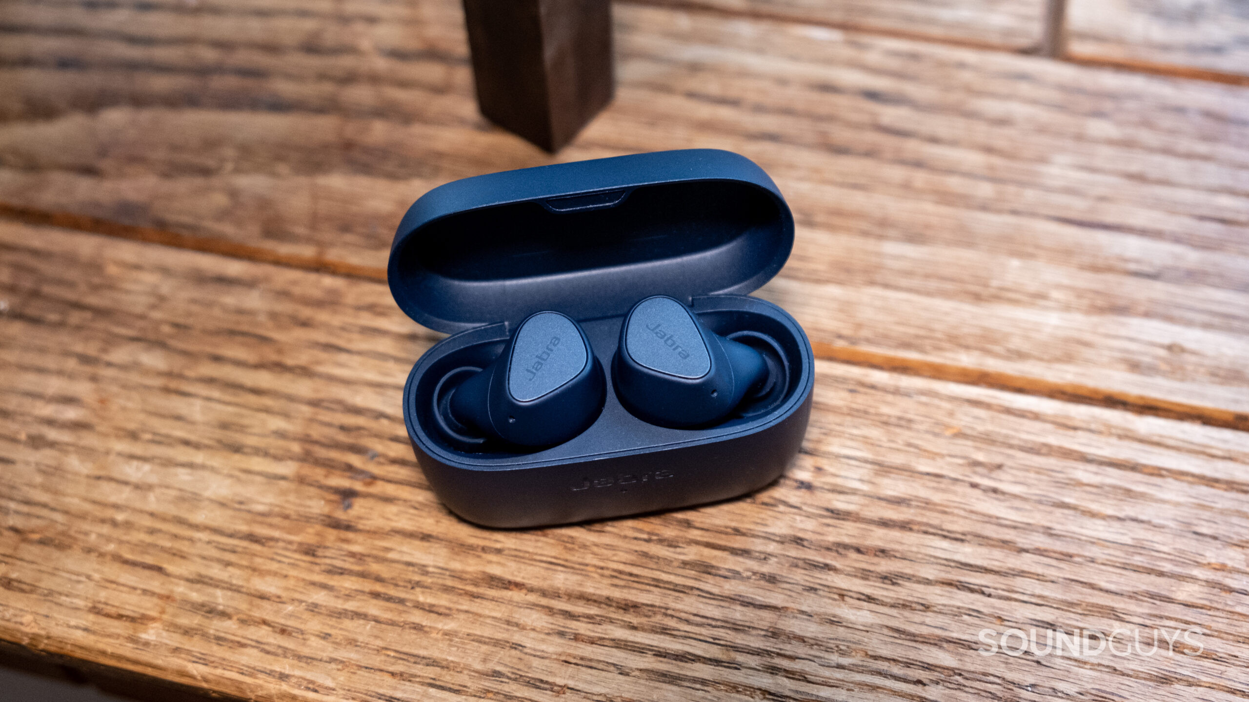 The Jabra Elite 4 sits on a wood surface with the case open showcasing the buds.