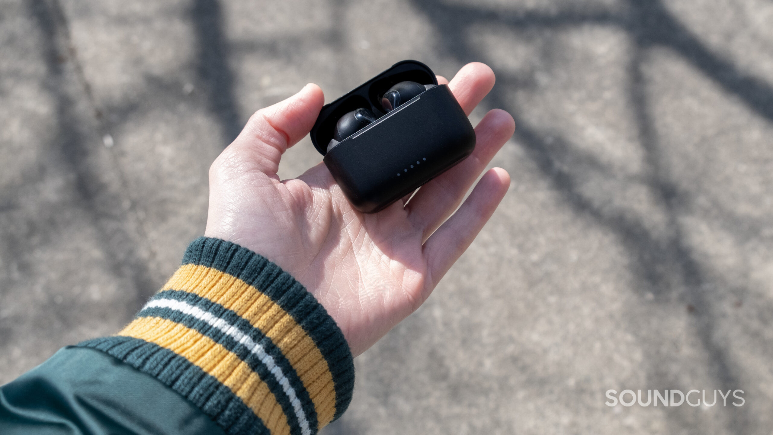 A hand holds the open TOZO NC2 case above a sidewalk.